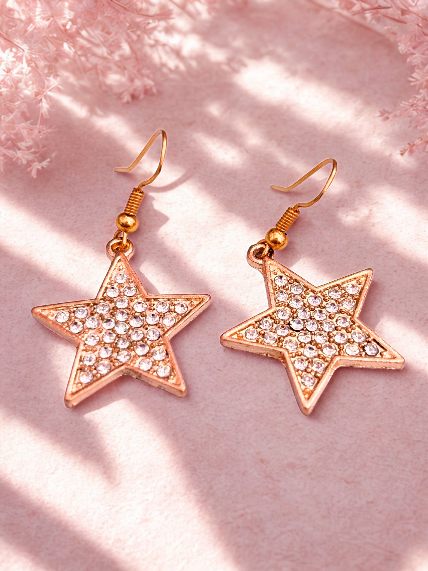 Star-shaped earrings with gold finish and clear stones on a pink background