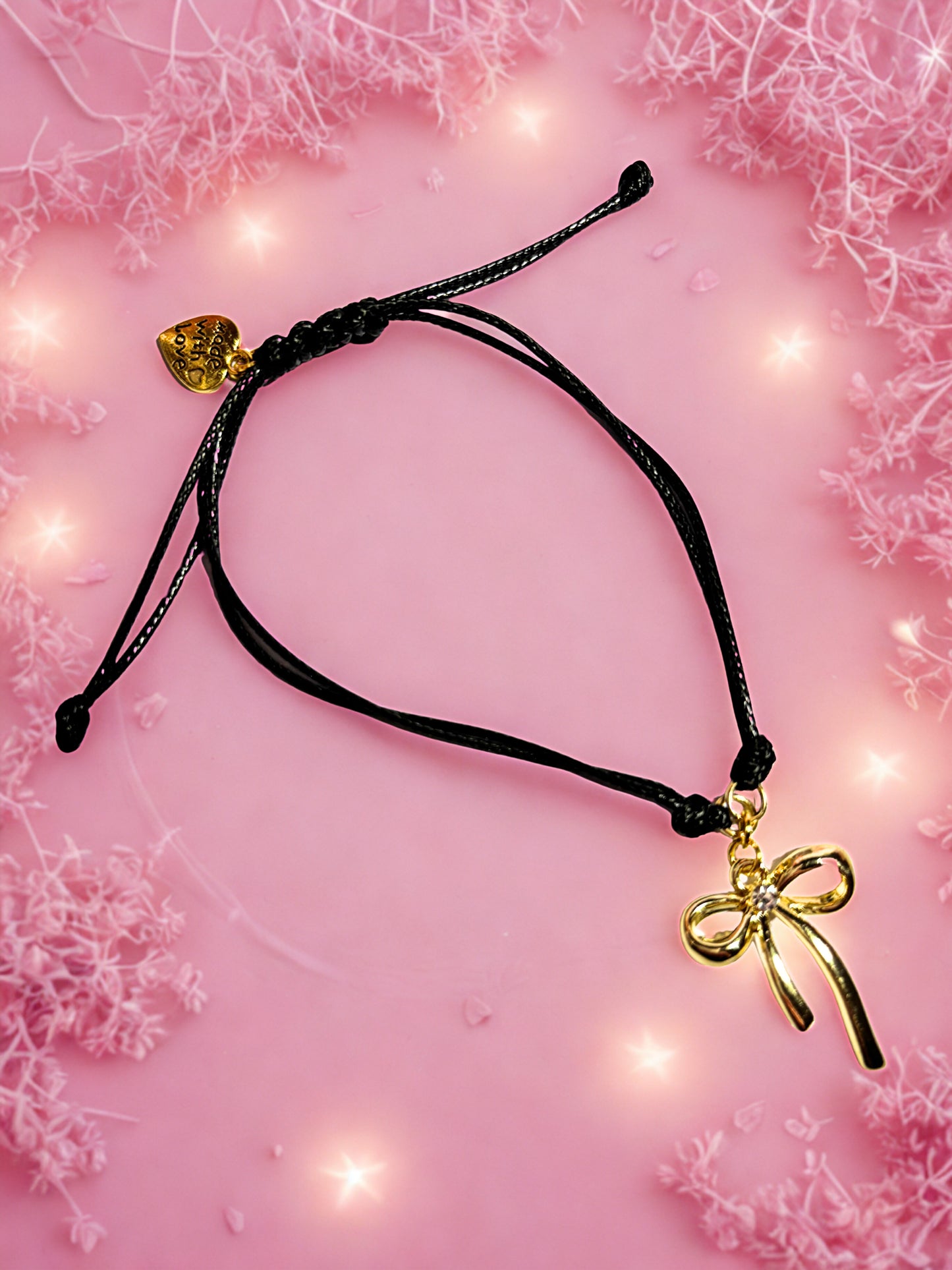 Black cord bracelet with gold bow charm on a pink floral background
