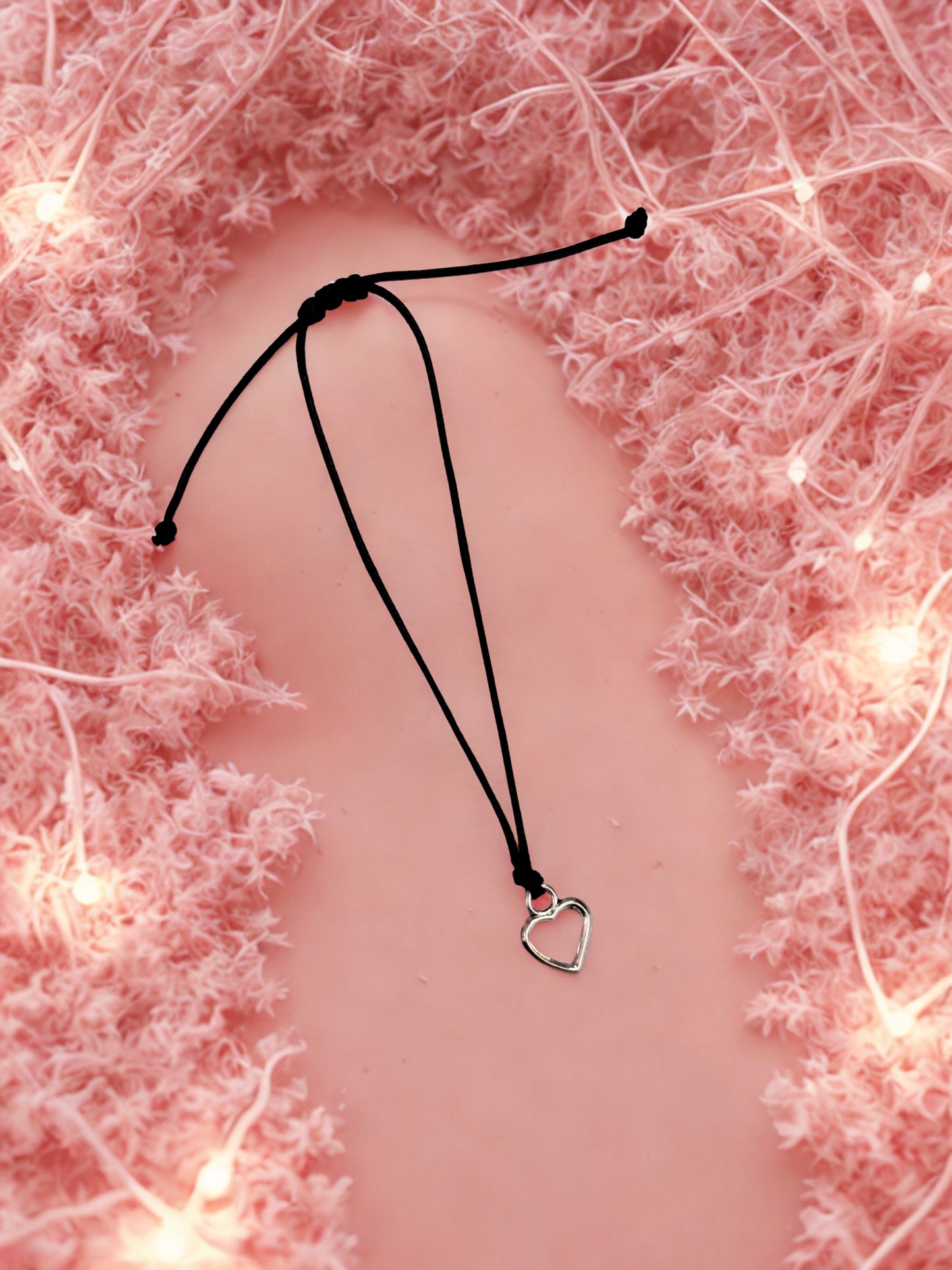Heart charm on a black cord bracelet on a pink background