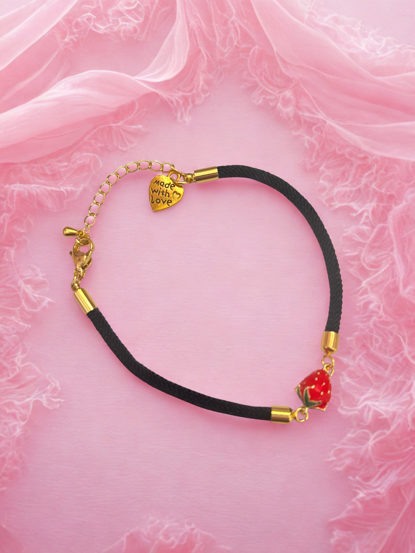 Bracelet with strawberry charm on a pink fabric background