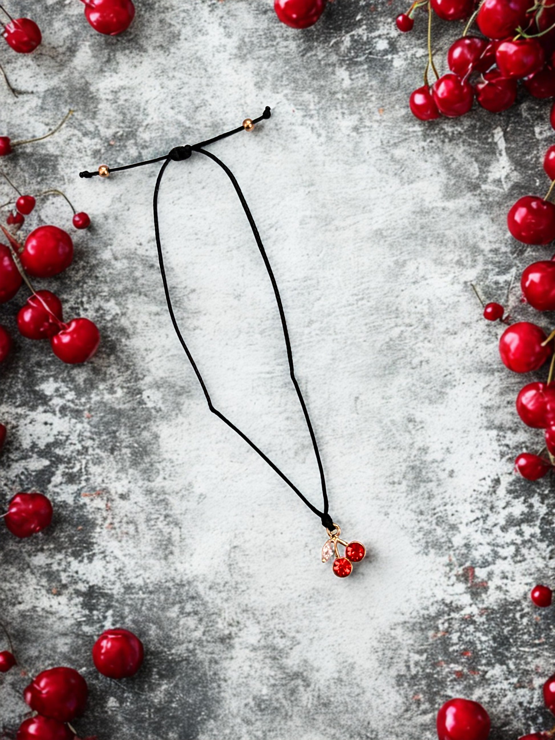 Black bracelet with red cherry charm on a grey surface surrounded by red berries