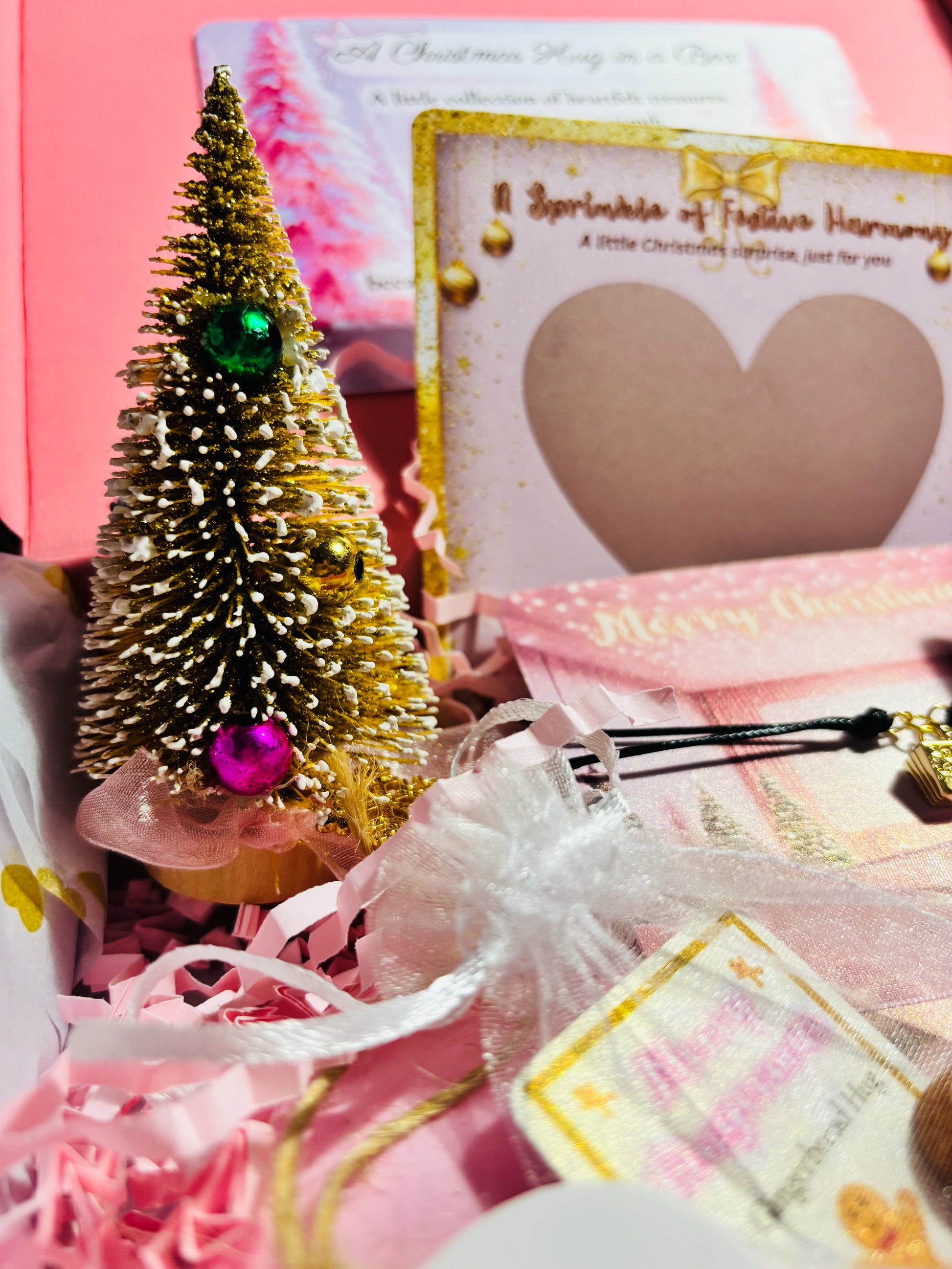 Small decorative Christmas tree with pink ornament on a pink background with cards and ribbons.
