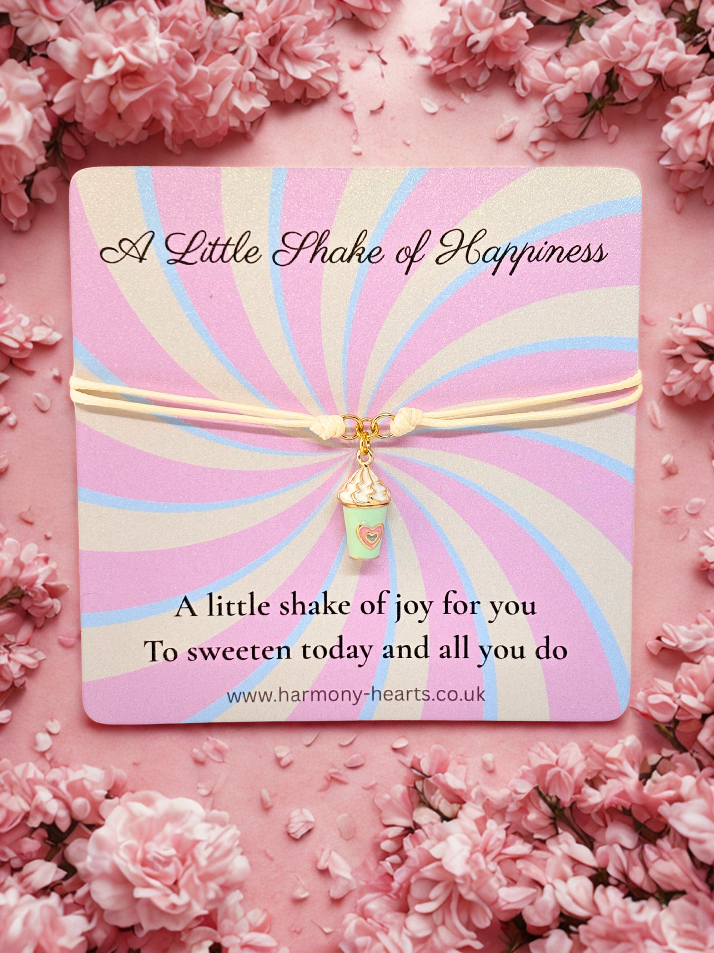 Branded Card with 'A Little Shake of Happiness' message and a milkshake charm bracelet with decorative elements on a pink floral background