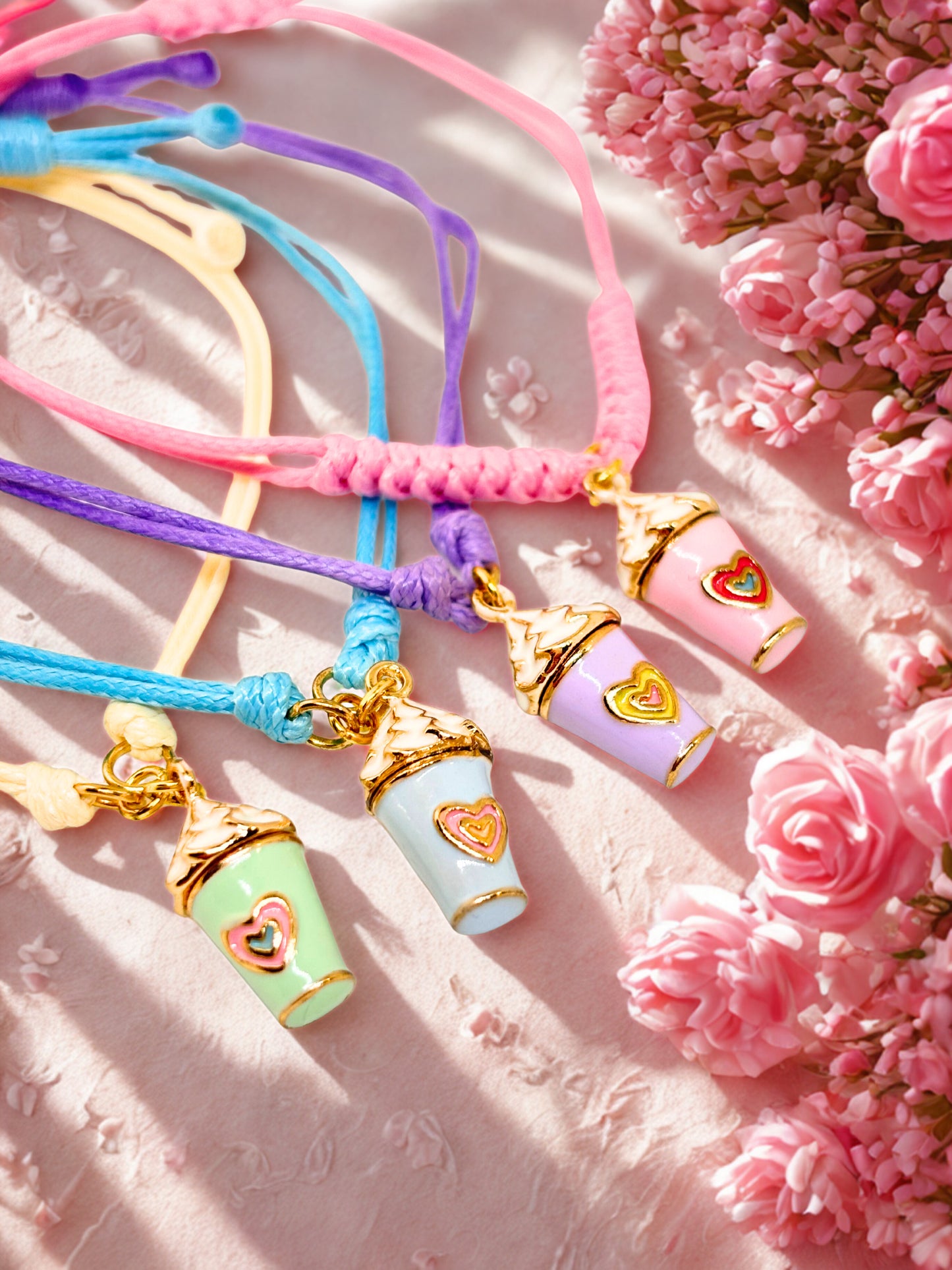 Colourful bracelets with enamel milkshake charms on a pink floral background