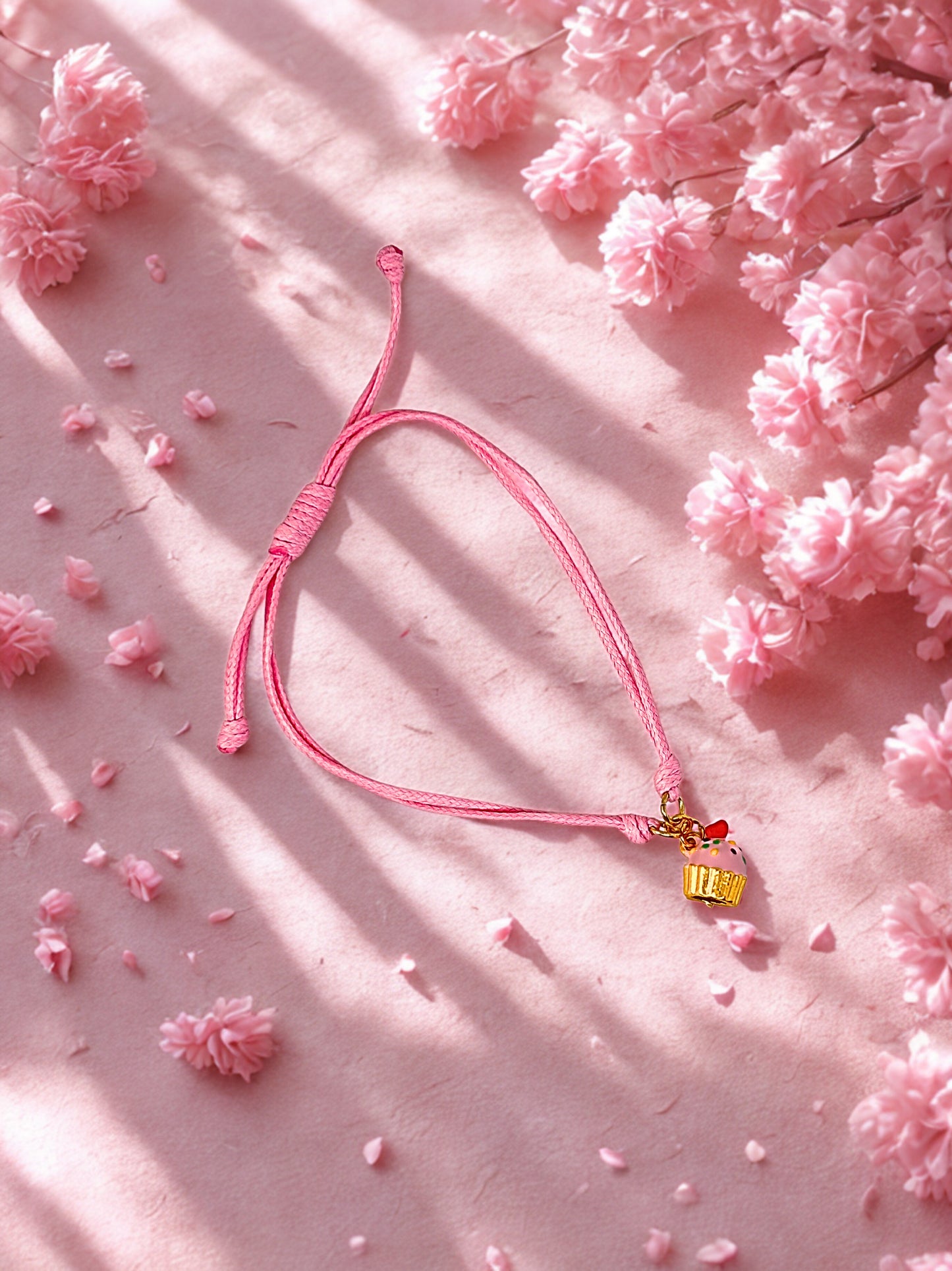 Pink bracelet with a small gold cupcake charm on a pink floral background