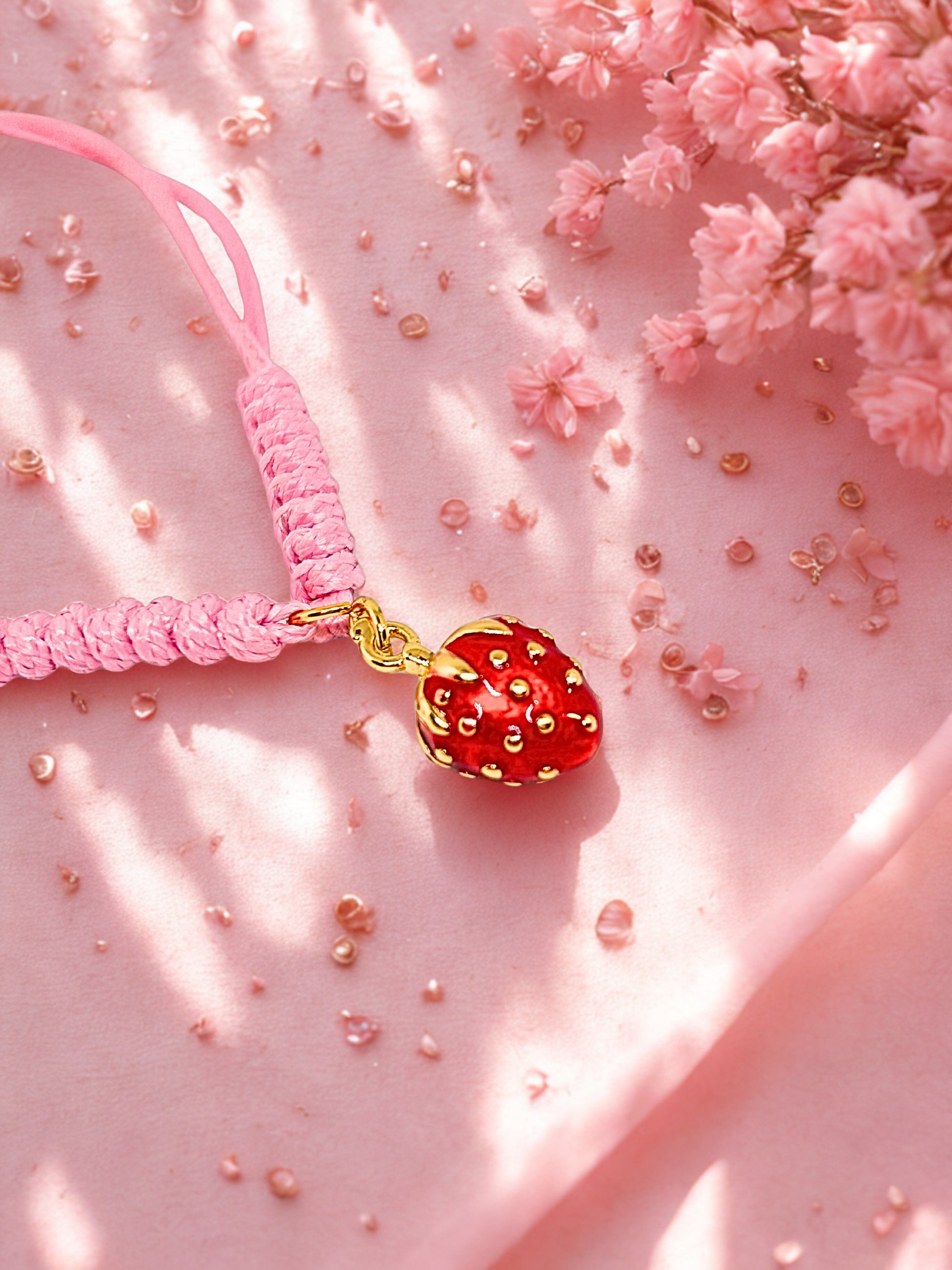 Pink cord bracelet with a red and gold strawberry charm