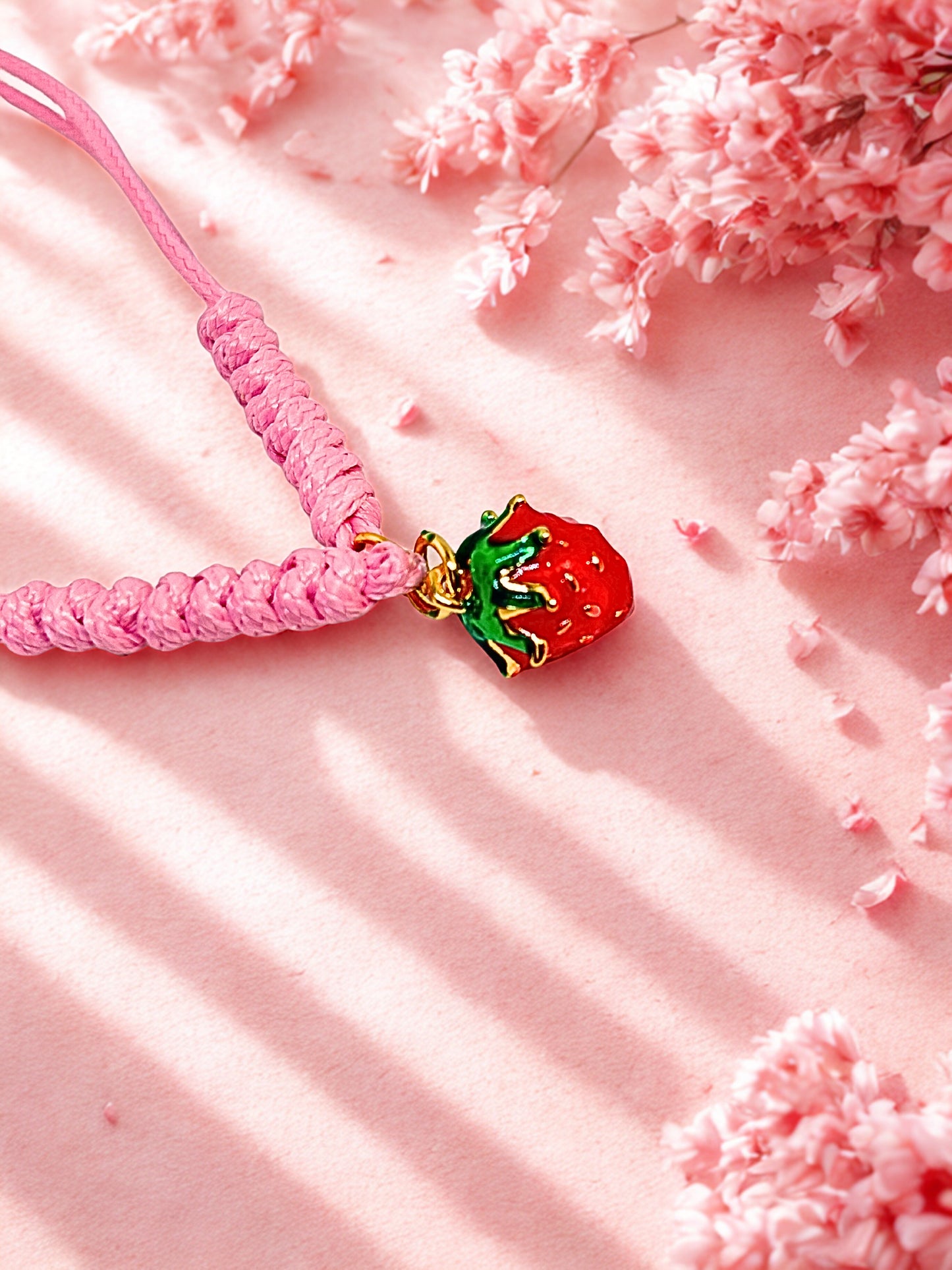 Pink cord bracelet with a red gold and green strawberry charm