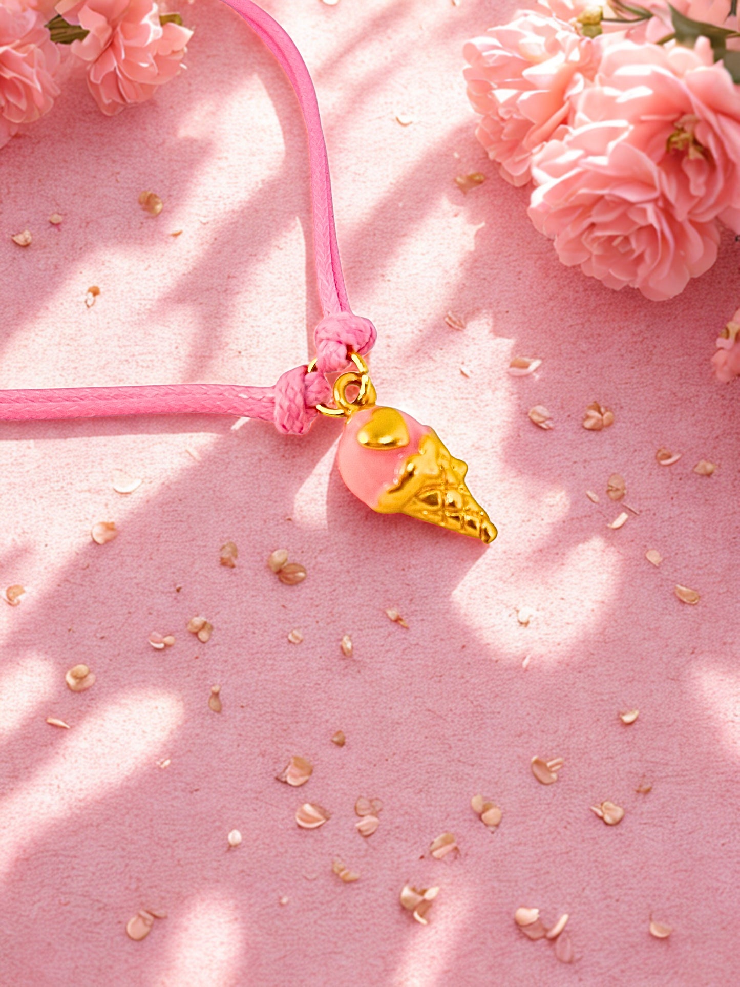Pink charm bracelet with a gold ice cream cone charm on a pink background with flowers and petals.