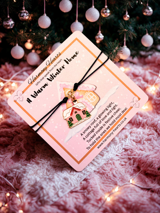 Pink charm bracelet on a Christmas-themed card with a house ornament on a pink background, surrounded by festive decorations.