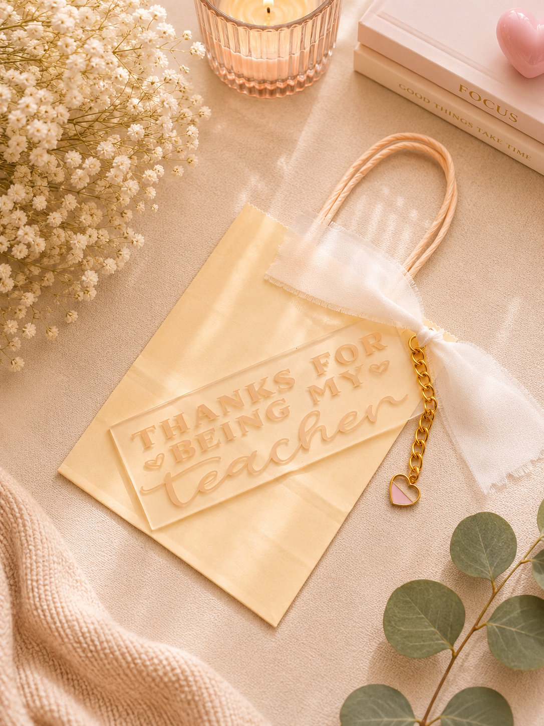 Gift bag and bookmark with 'Thanks for being my teacher' card on a decorative surface with flowers and candles.