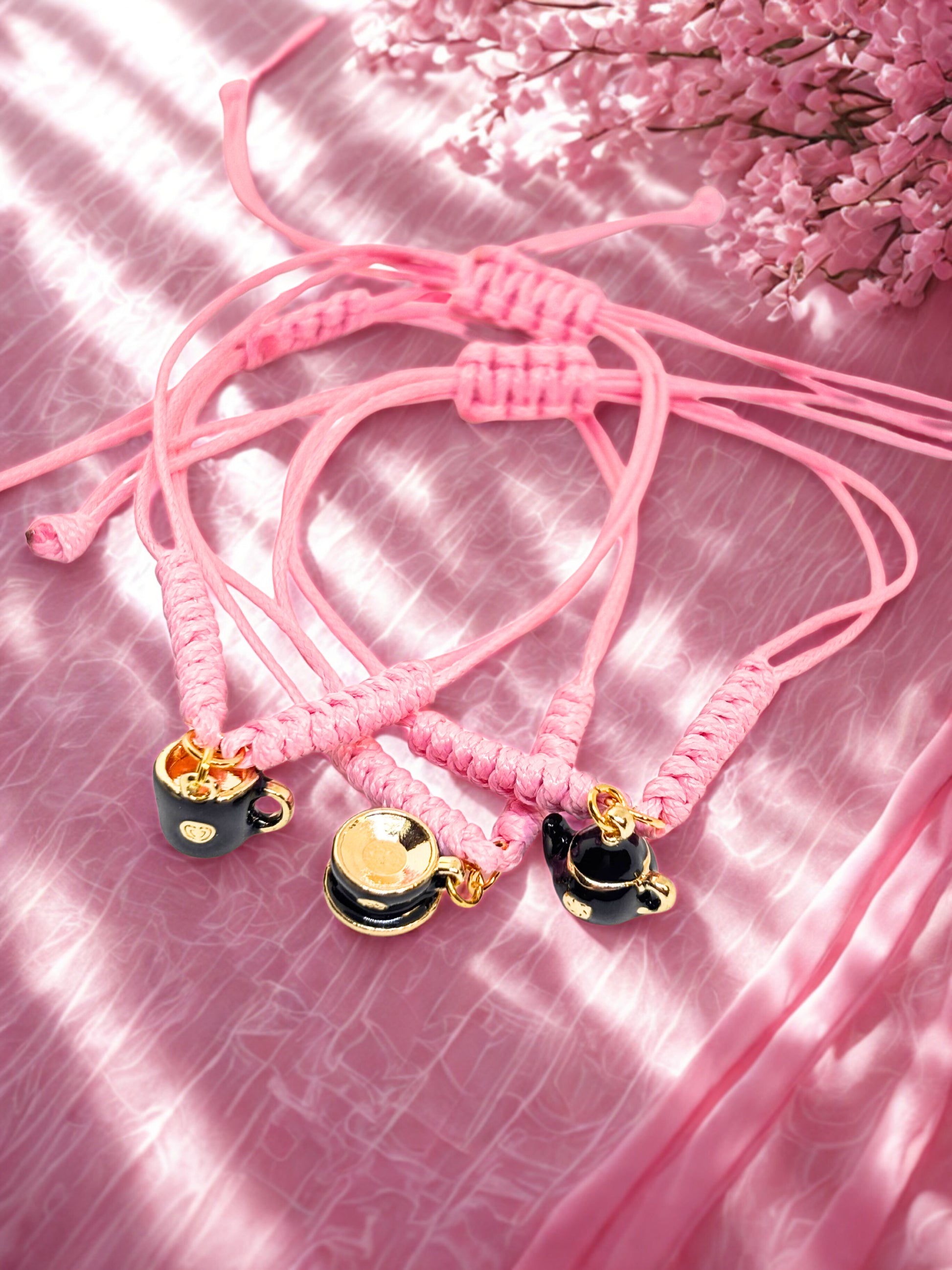 Pink braided bracelets with black and gold teapot and teacup charms on a pink textured background