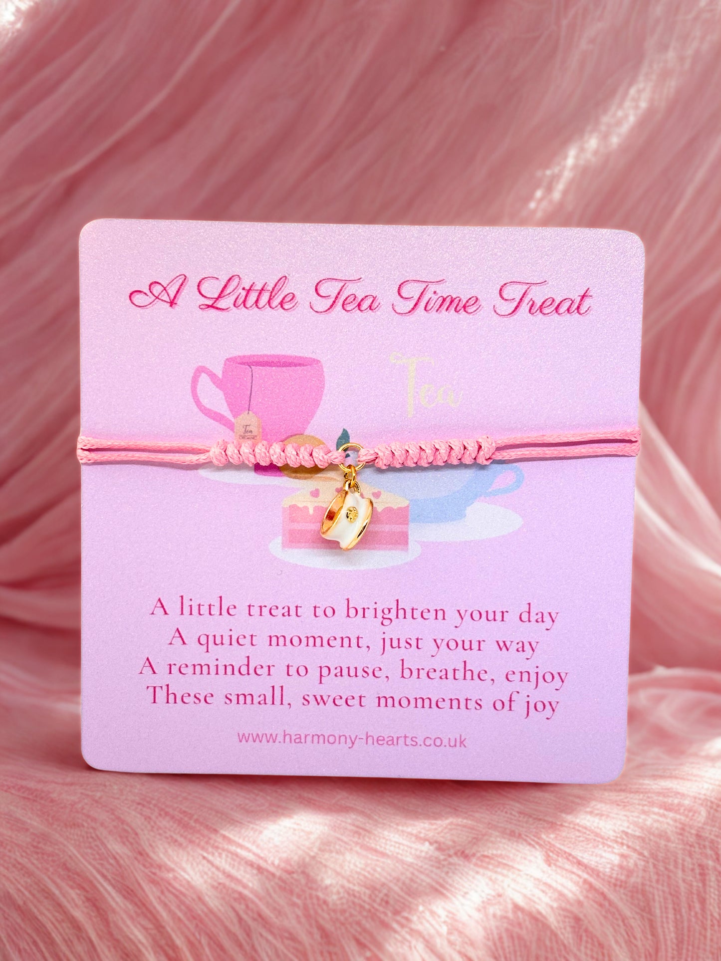Pink bracelet with teacup charm on a matching card with text, against a pink textured background.