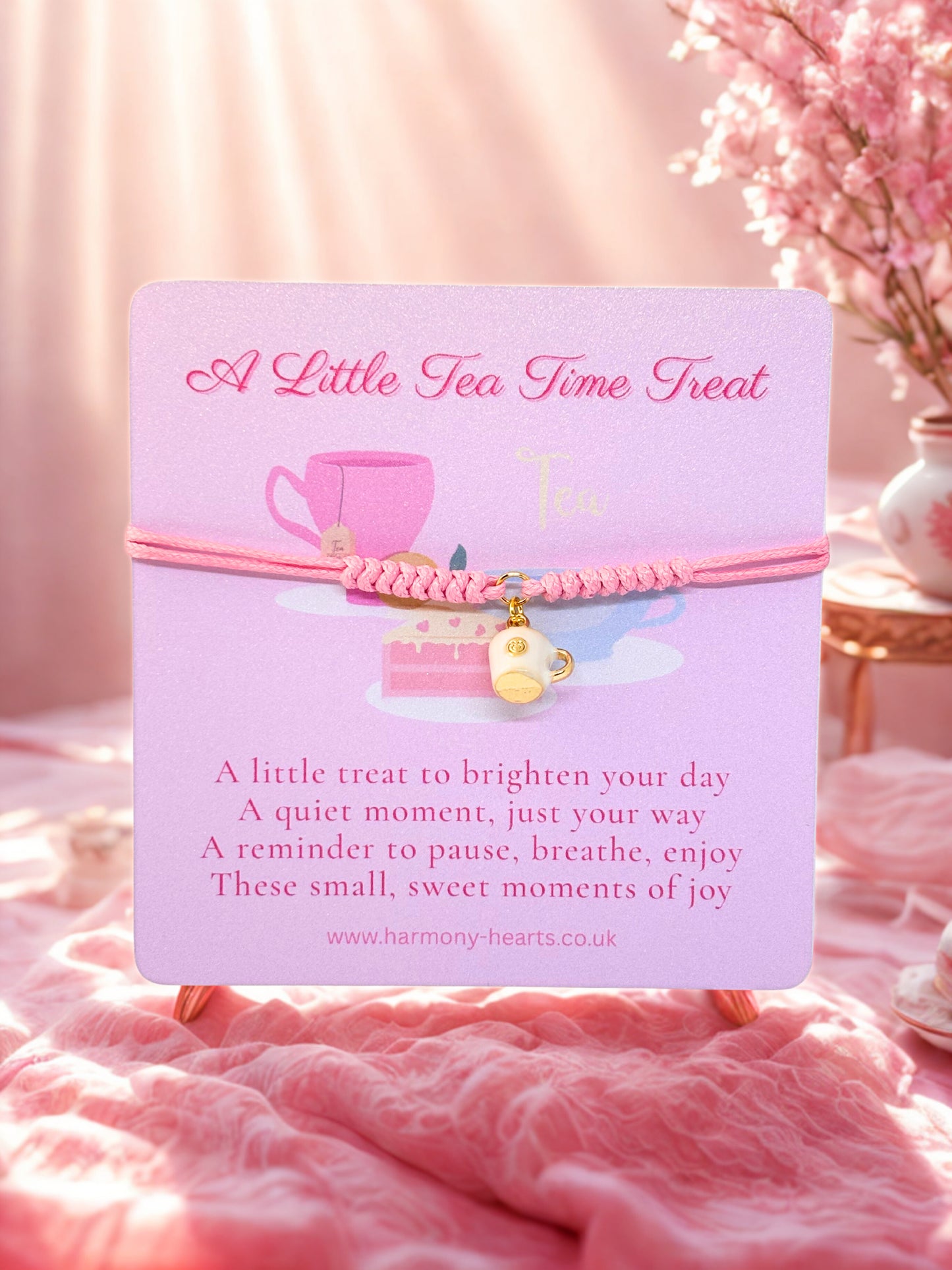 Pink bracelet with cup charm on a pink card with text, against a soft pink background.
