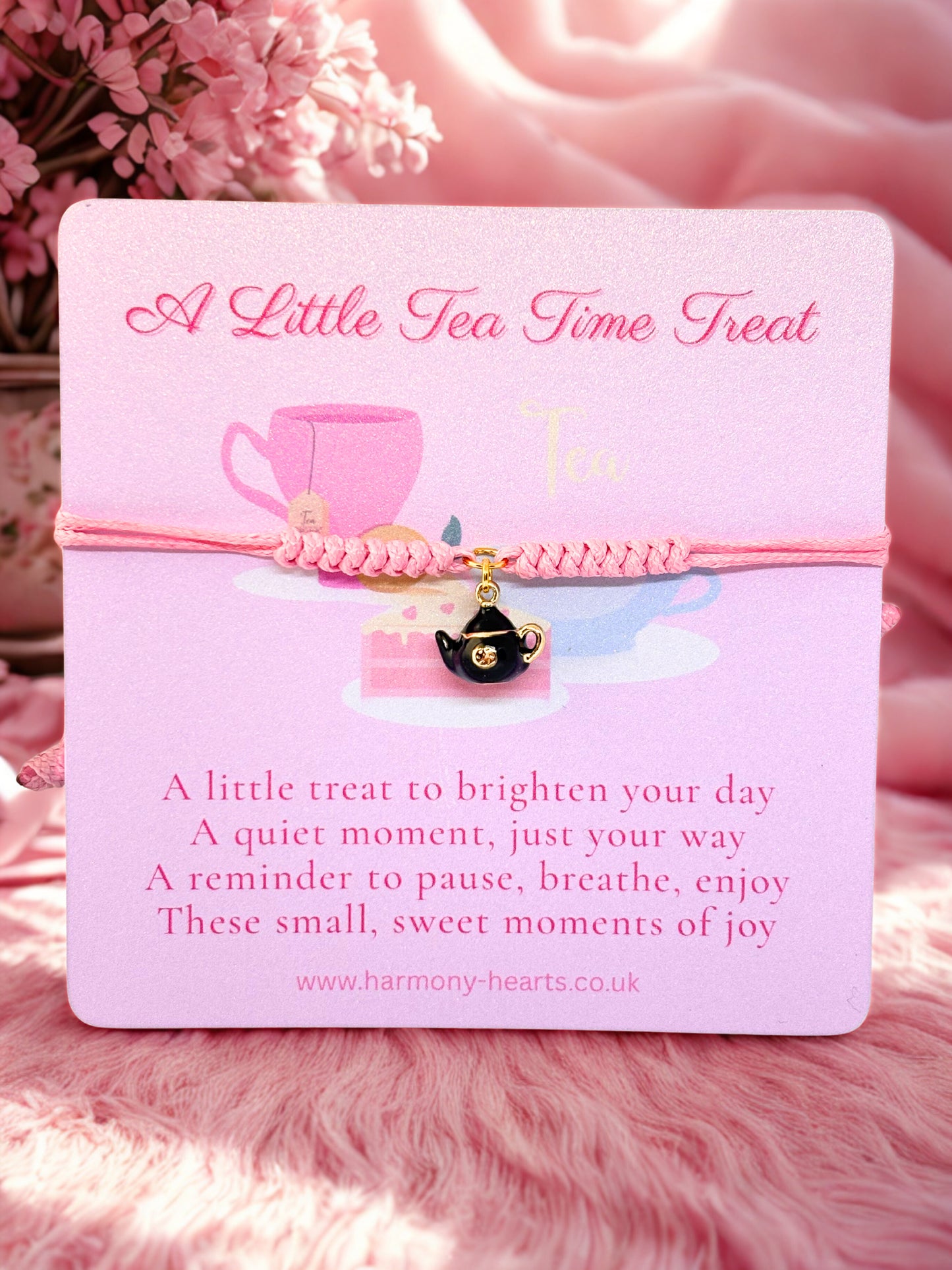Pink card with tea cup design and text on a pink background with a pink charm bracelet and teapot charm