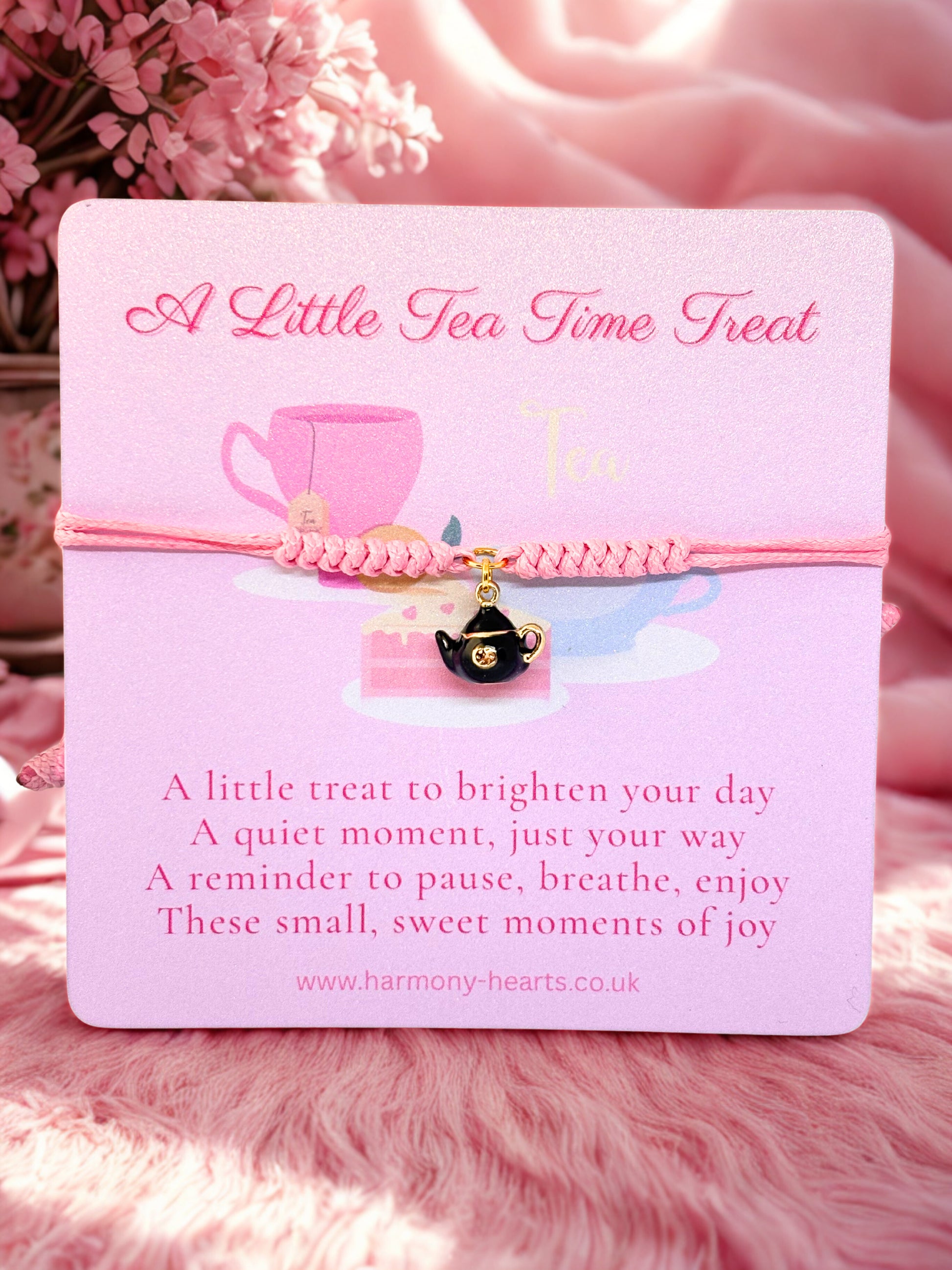 Pink card with tea cup design and text on a pink background with a pink charm bracelet and teapot charm