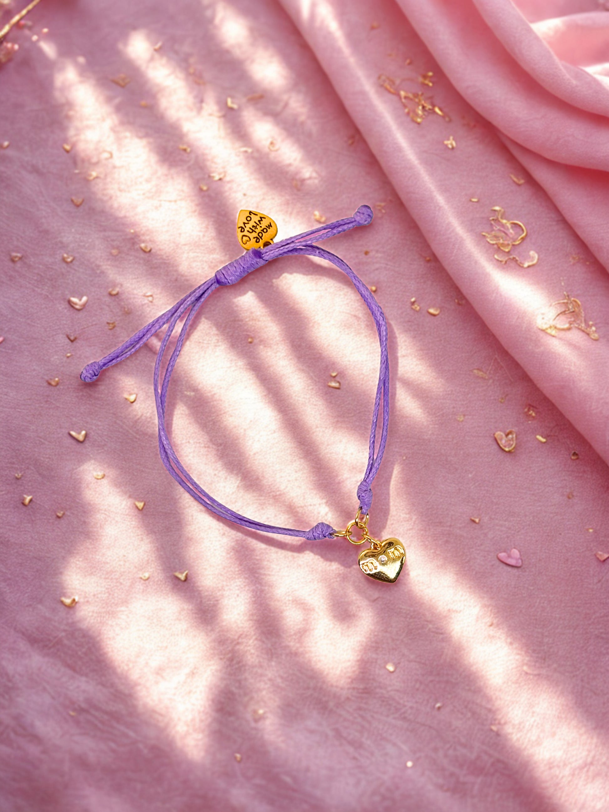 Purple bracelet with heart-shaped charms on a pink fabric background