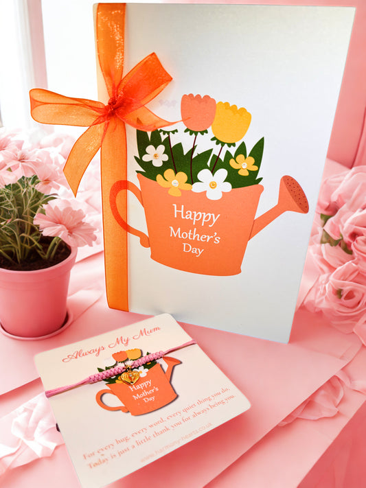 Mother's Day card with watering can design, flowers, and a matching gold heart charm bracelet on pink background