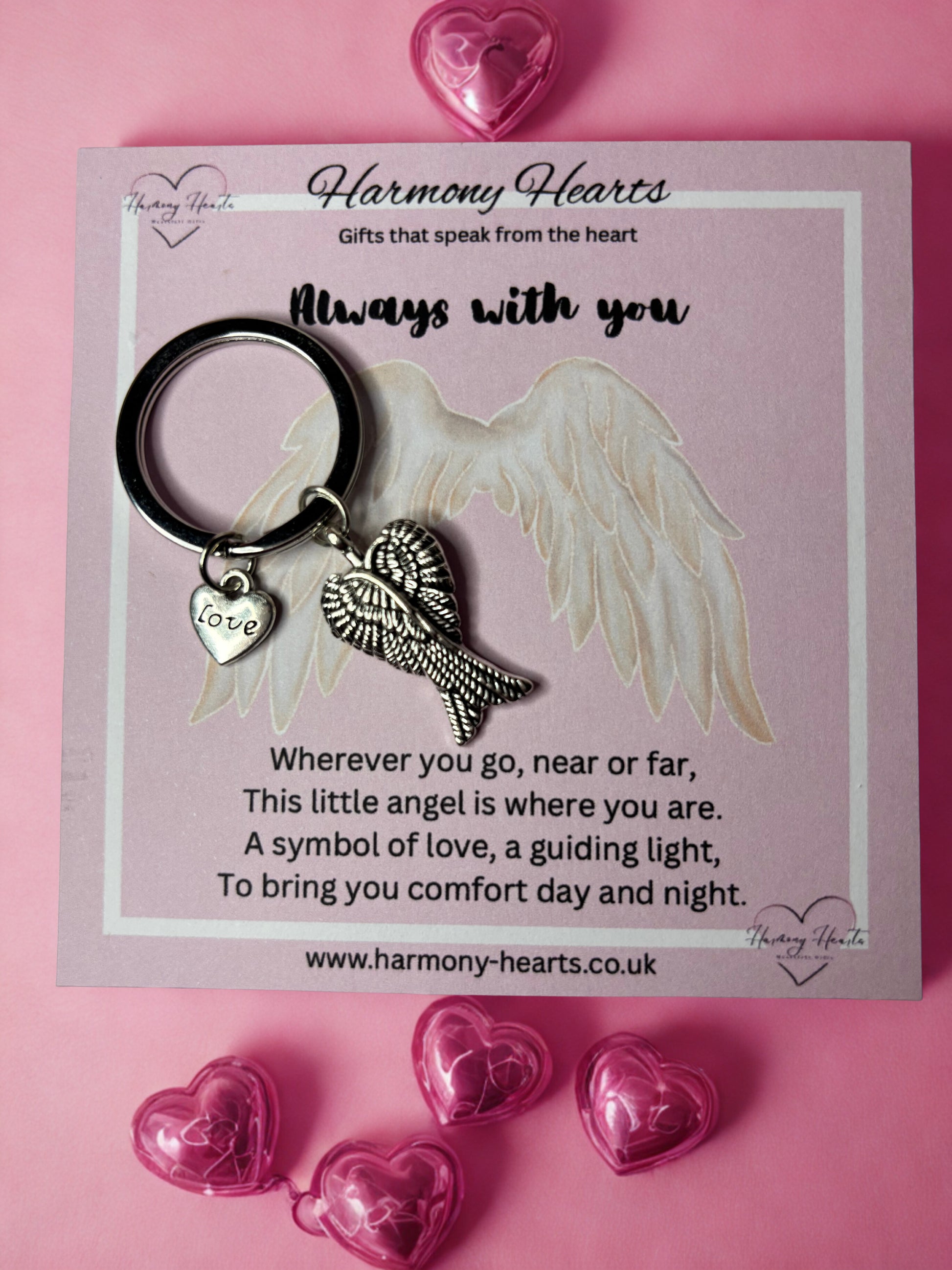 Keychain with angel wing and heart charm on a pink card with text, surrounded by pink hearts.
