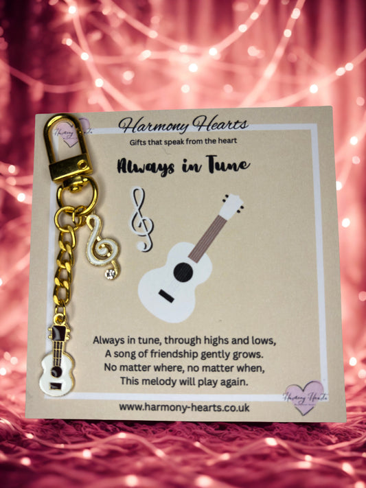 Keychain with ukulele and treble clef design on a Harmony Hearts card with a pink string background.