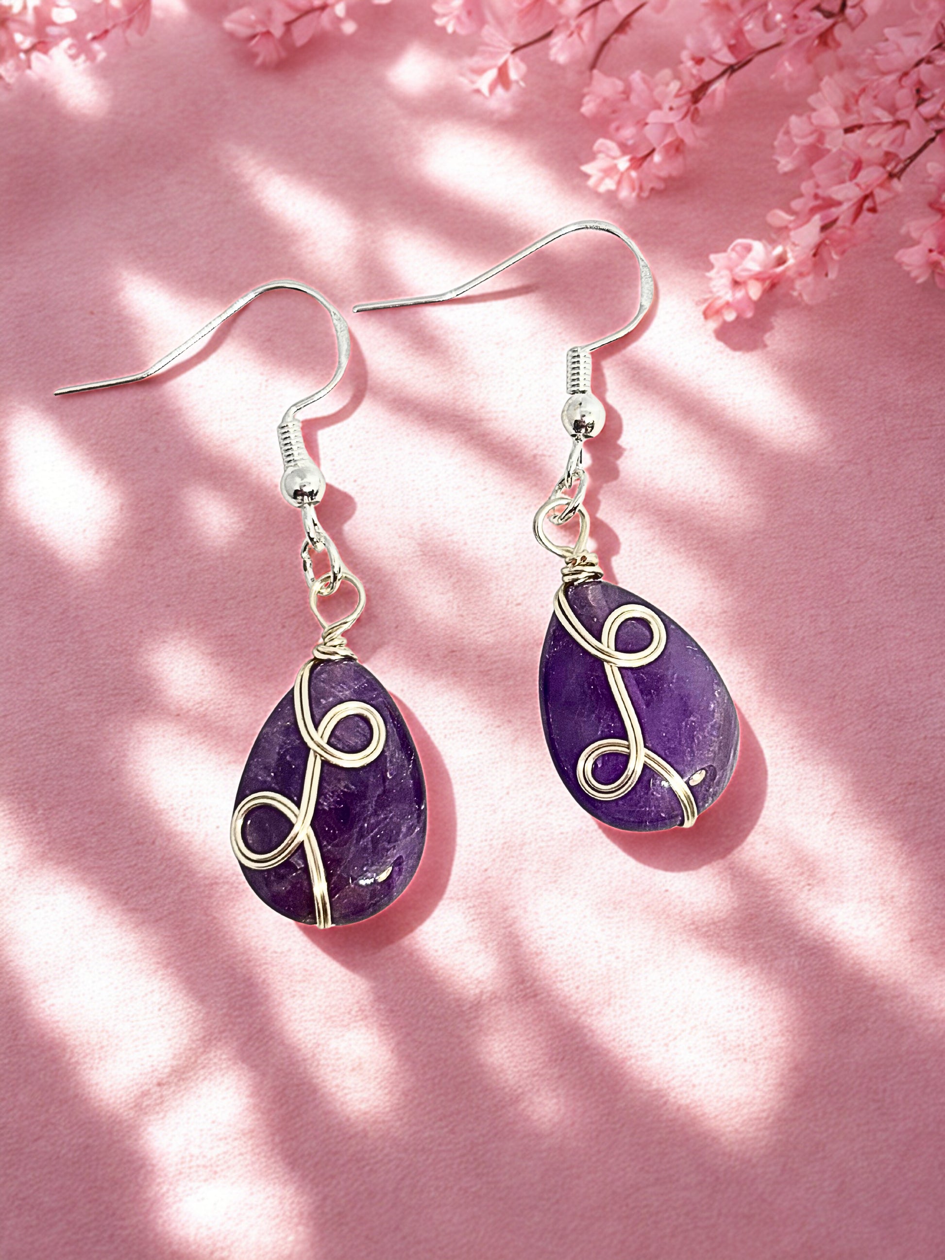 Amethyst teardrop earrings with silver wire wrapping on a pink background with cherry blossoms.