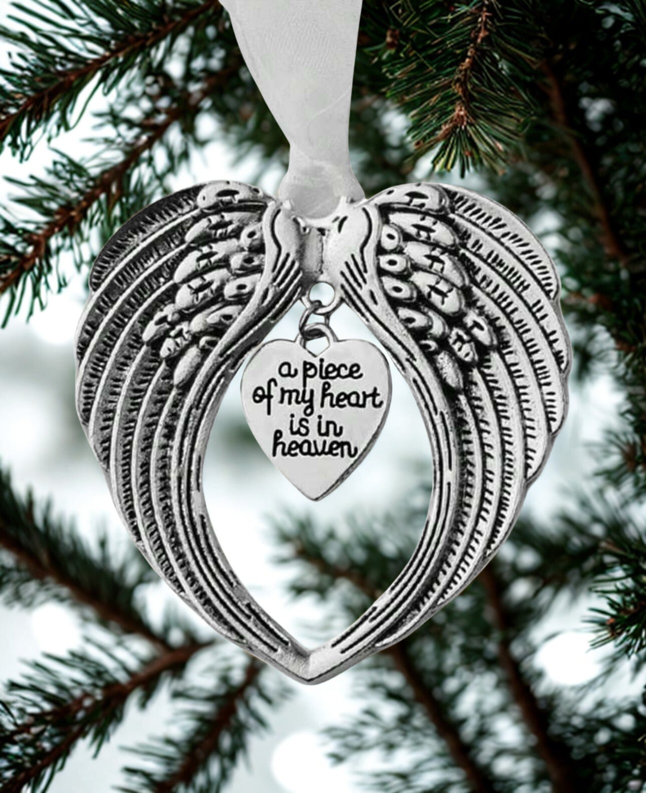 Decorative angel wing ornament with 'a piece of my heart is in heaven' message on a tree branch.