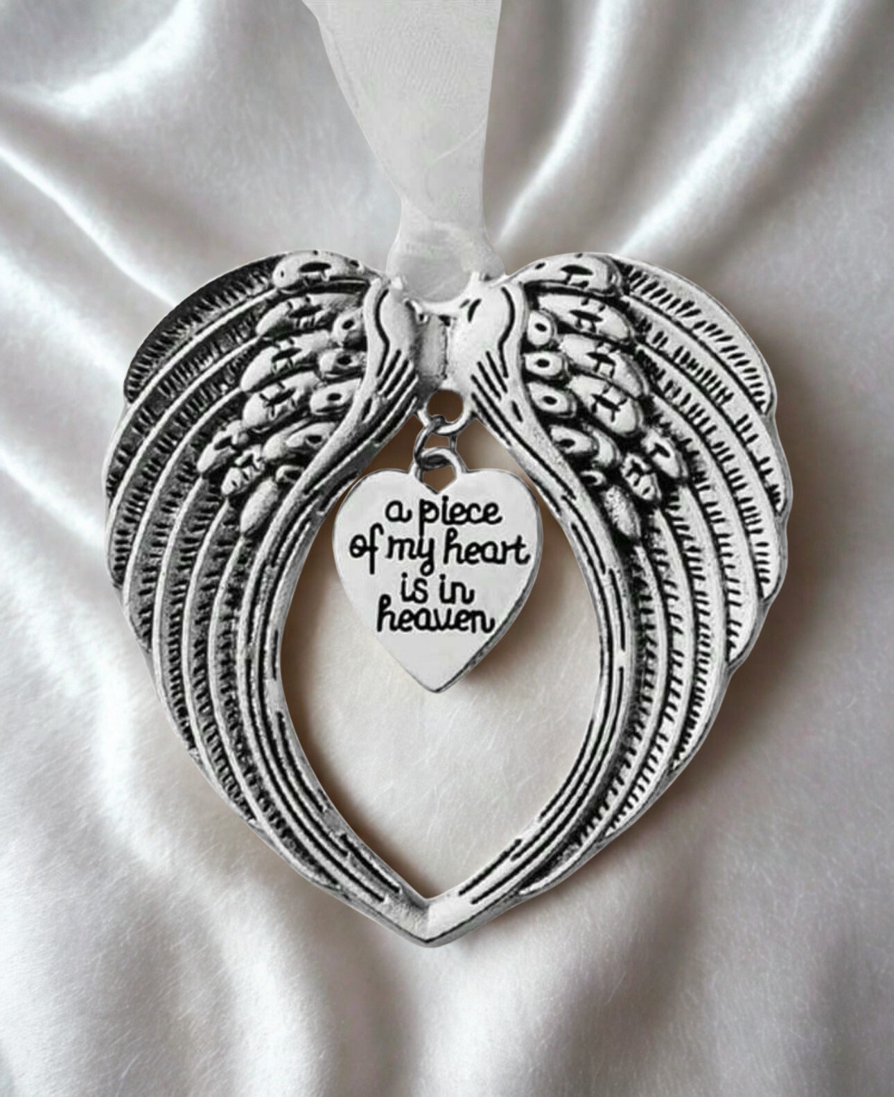 Silver angel wing pendant with heart-shaped tag on white fabric