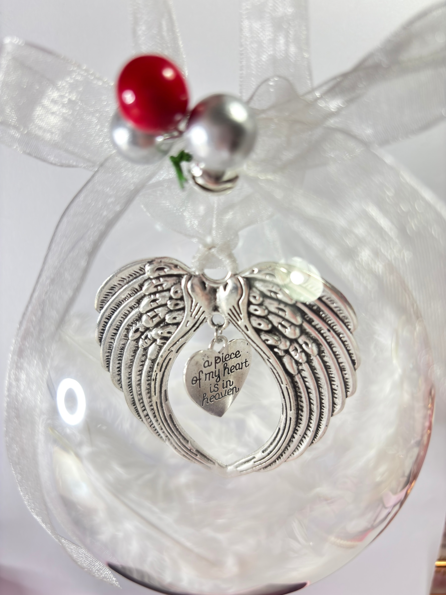 Decorative christmas bauble ornament with angel wing charm and red bead on a white background