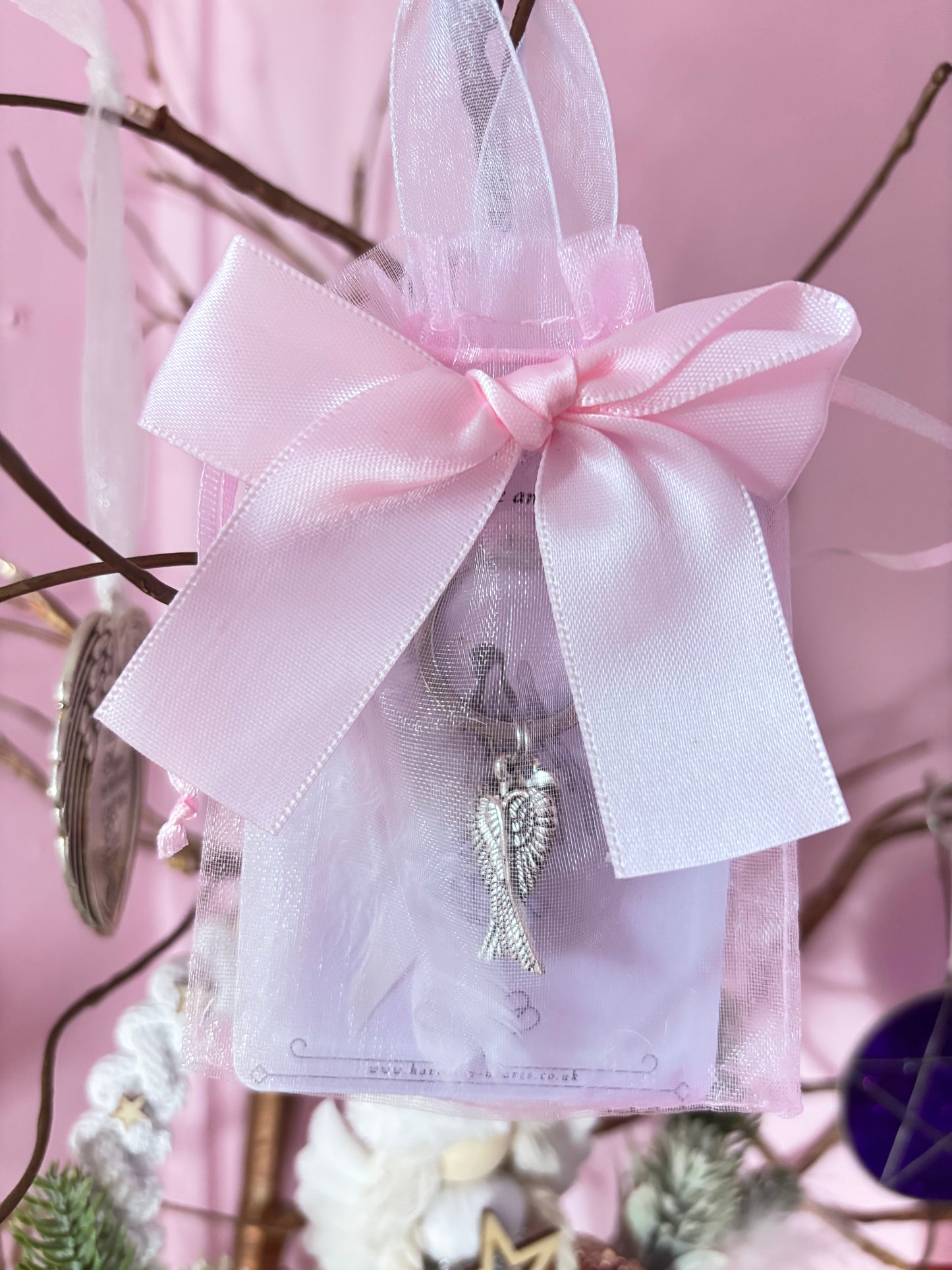 Decorative angel charm on a pink ribbon against a pink background