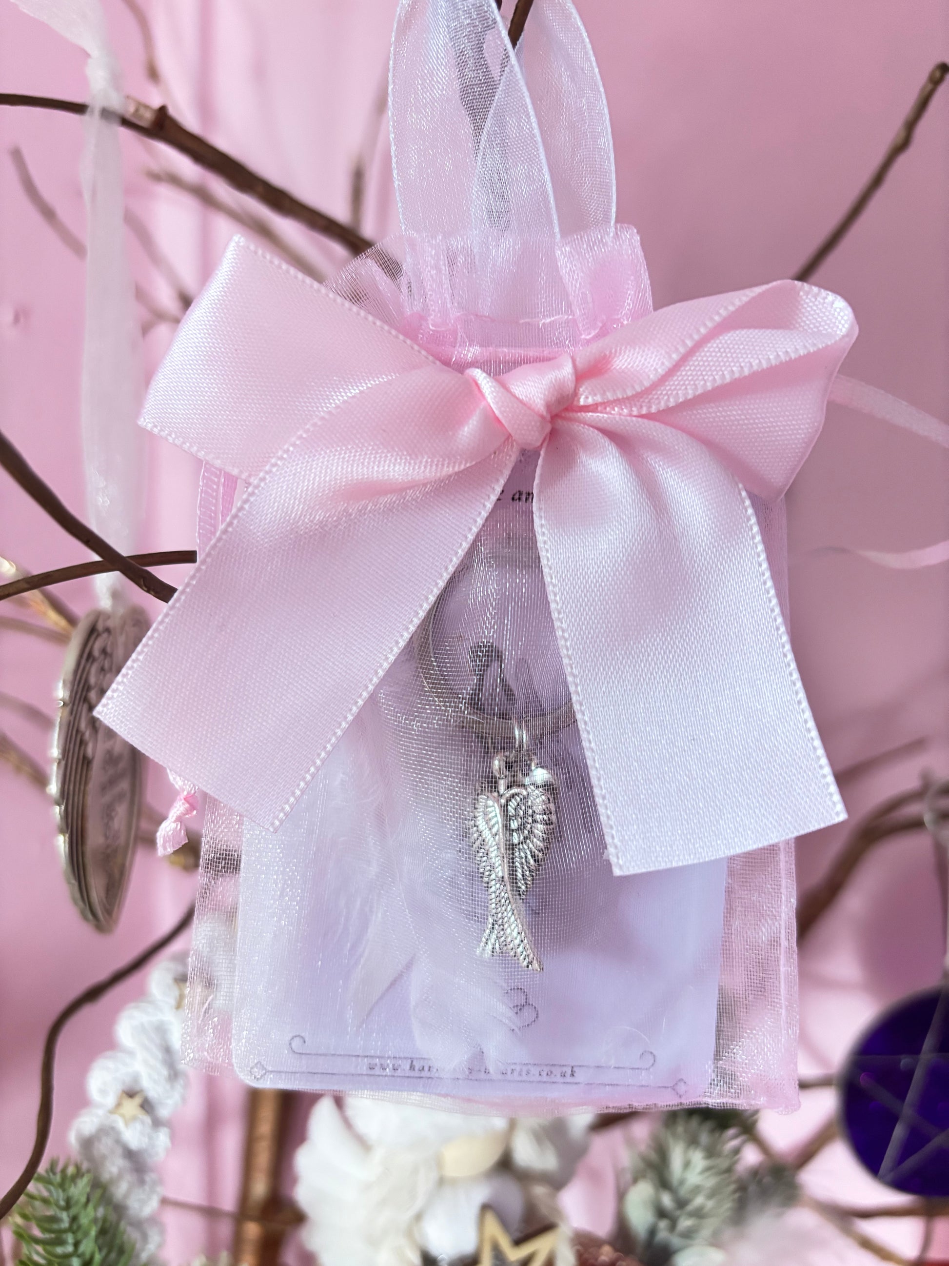 Decorative angel charm on a pink ribbon against a pink background