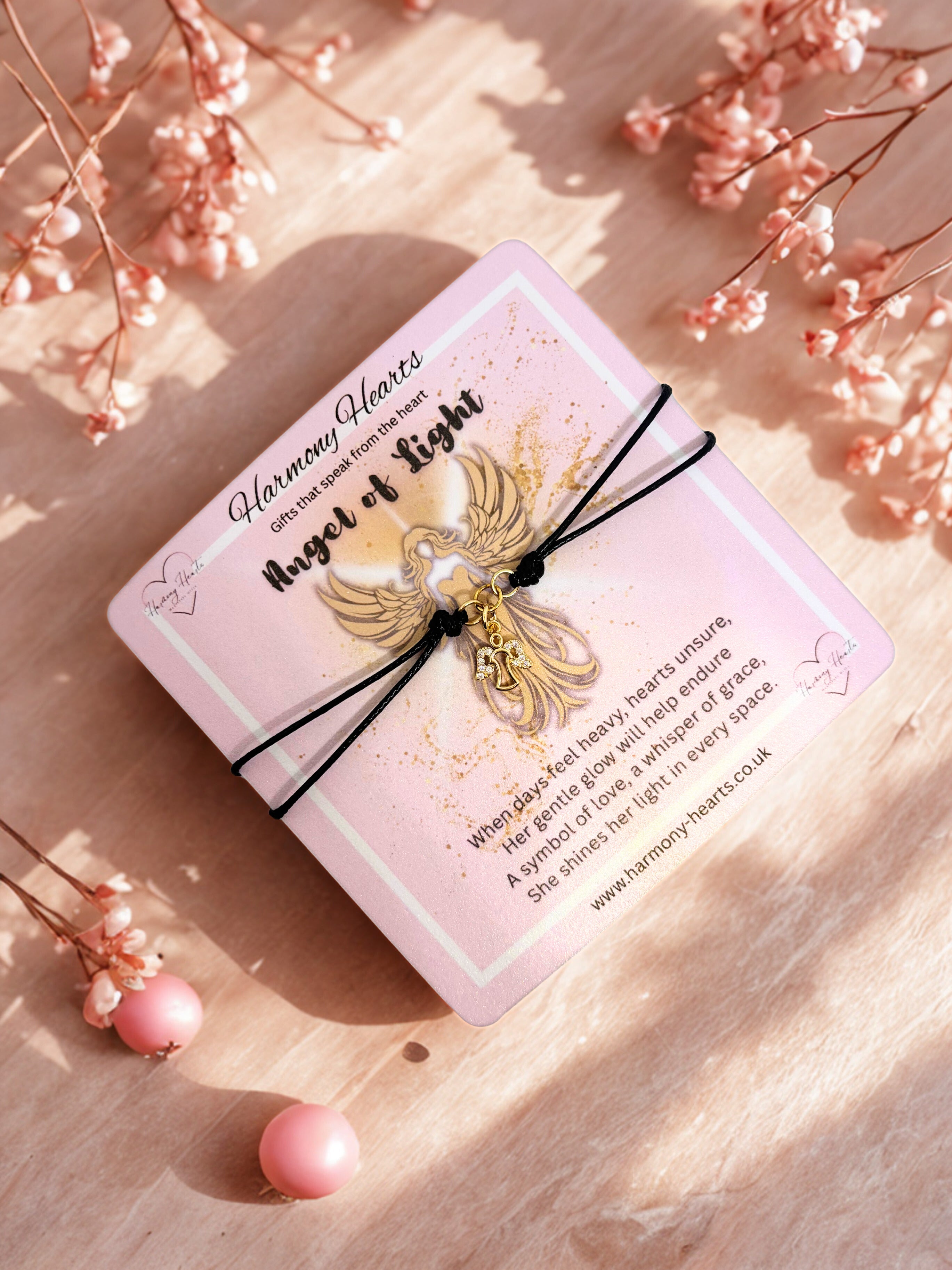 Pink card with angel charm on a wooden surface with pink flowers.