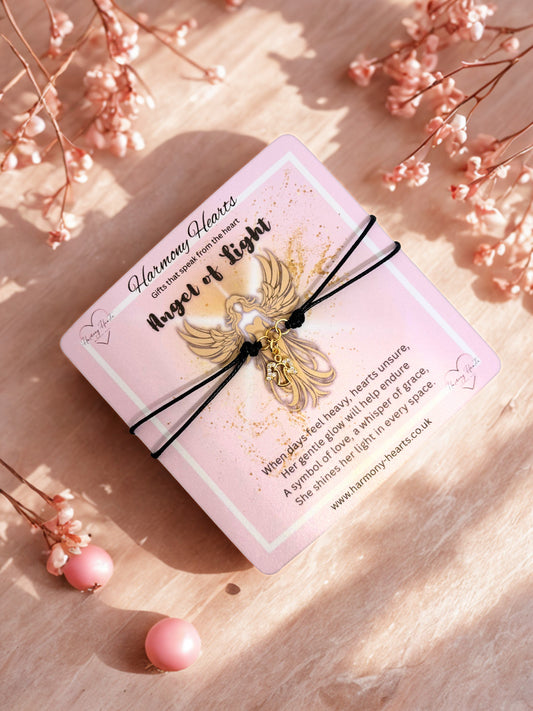 Pink card with angel charm on a wooden surface with pink flowers.