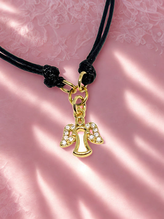 Gold angel charm on a black cord against a pink floral background