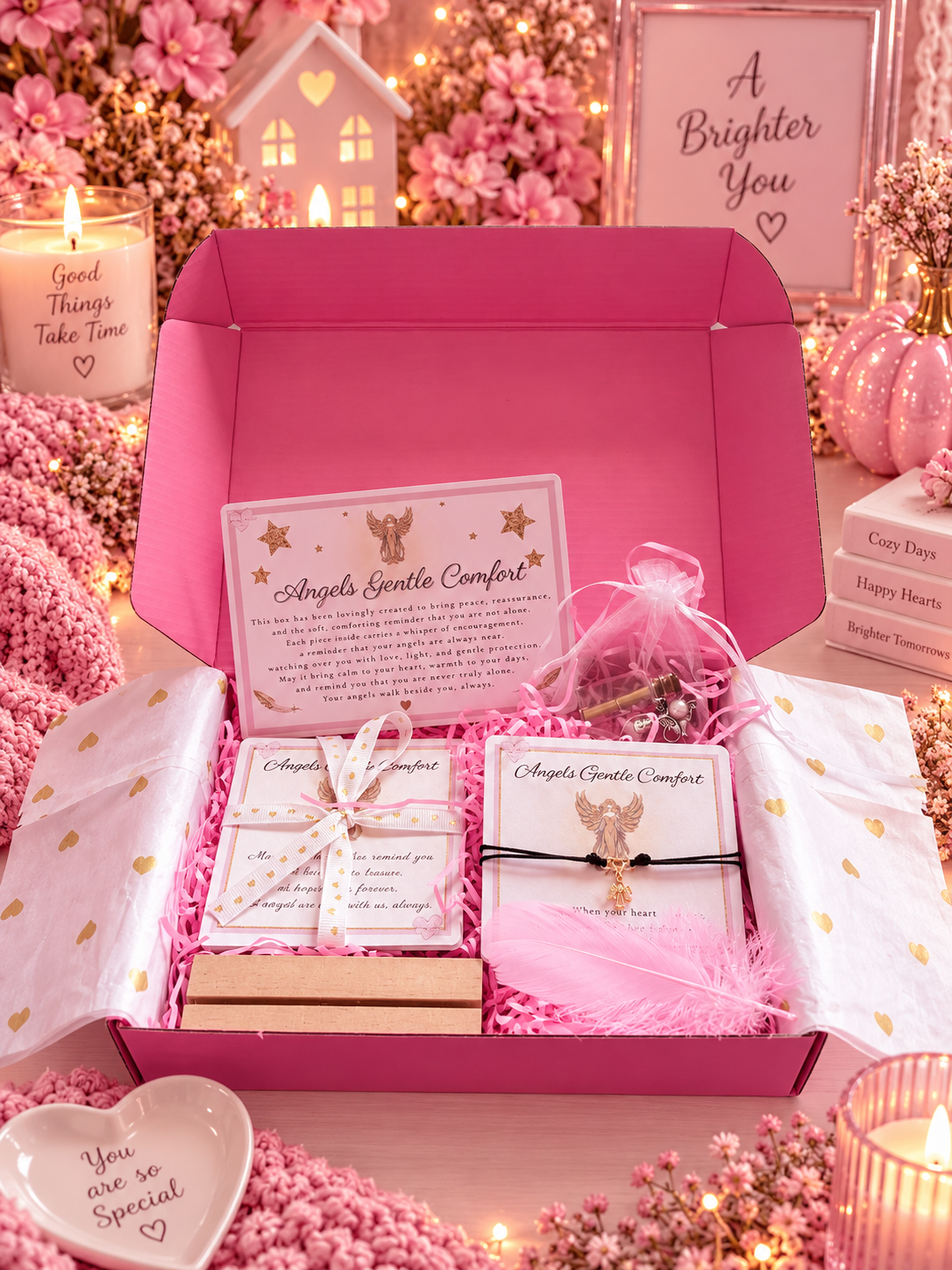A pink gift box filled with angel comfort items, including a bracelet, cards in a small wrapped box, styled with pink decorative props, candles, and fairy lights.