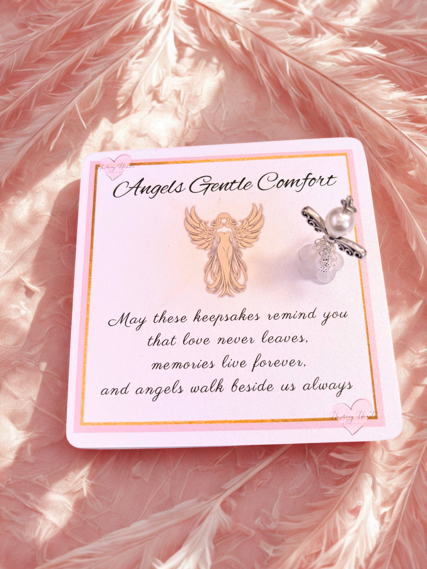 Decorative card with angel wings and heart charm on a pink feather background