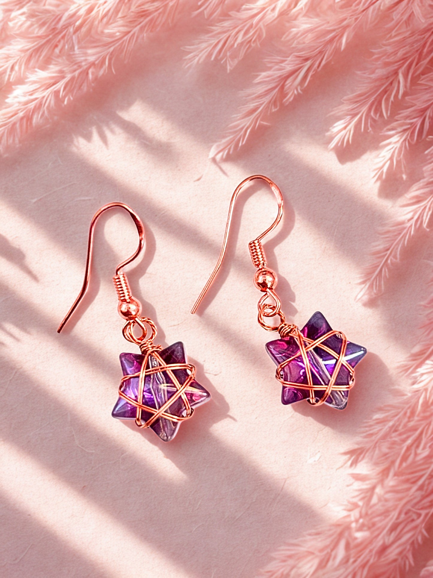 Pair of star-shaped earrings with purple and pink gemstones on a pink textured background