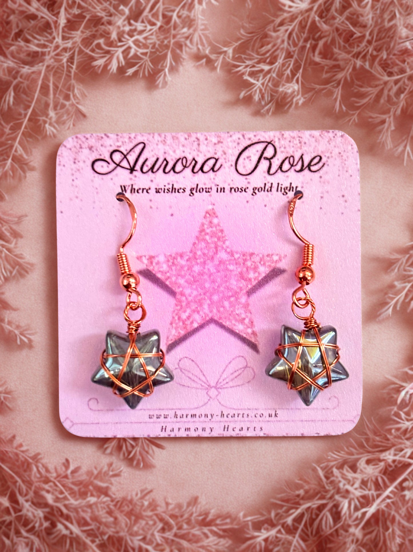 Star-shaped earrings on a 'Aurora Rose' branded card with a pink background
