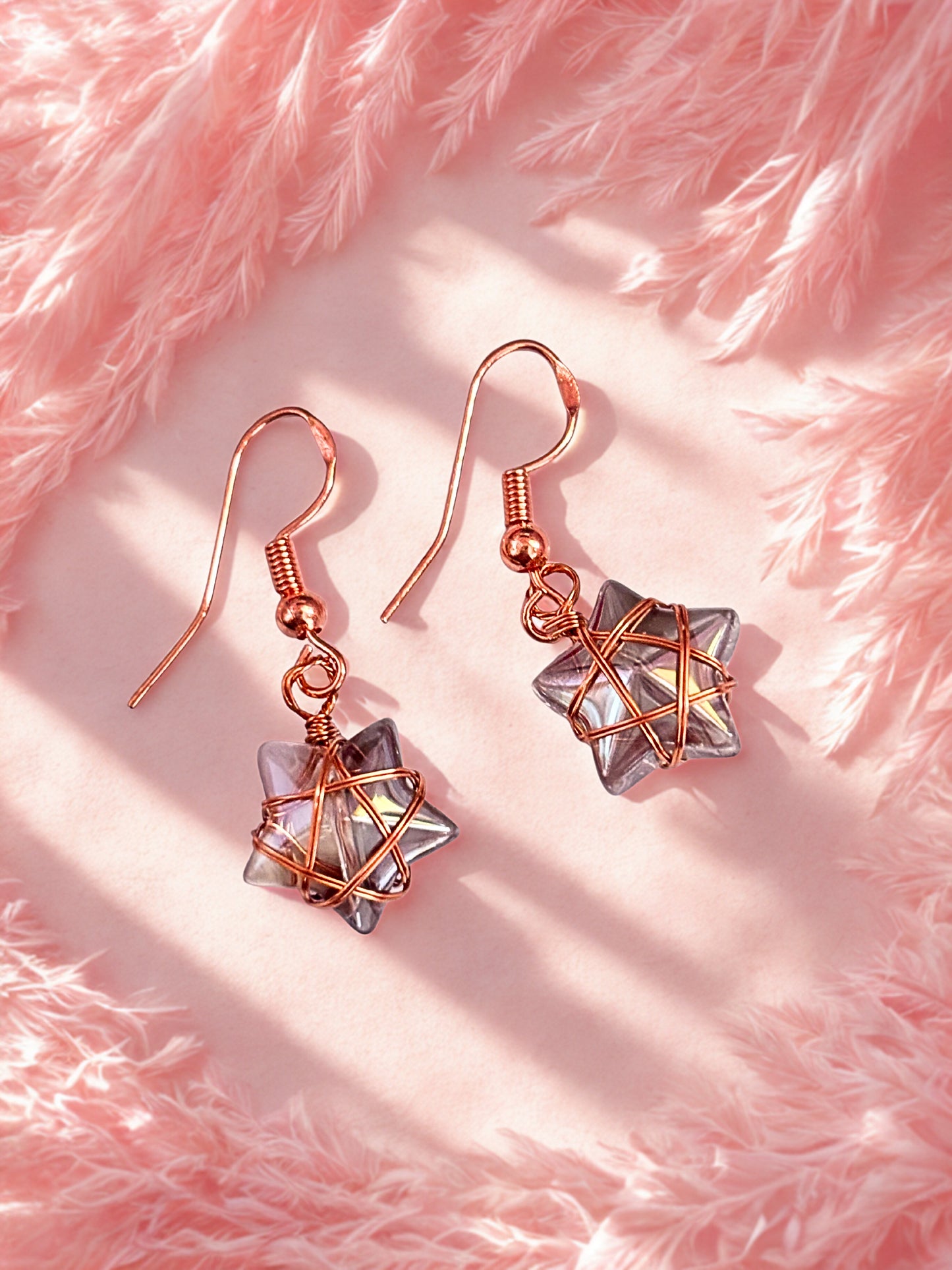 Rose gold earrings with star-shaped designs on a pink fluffy background
