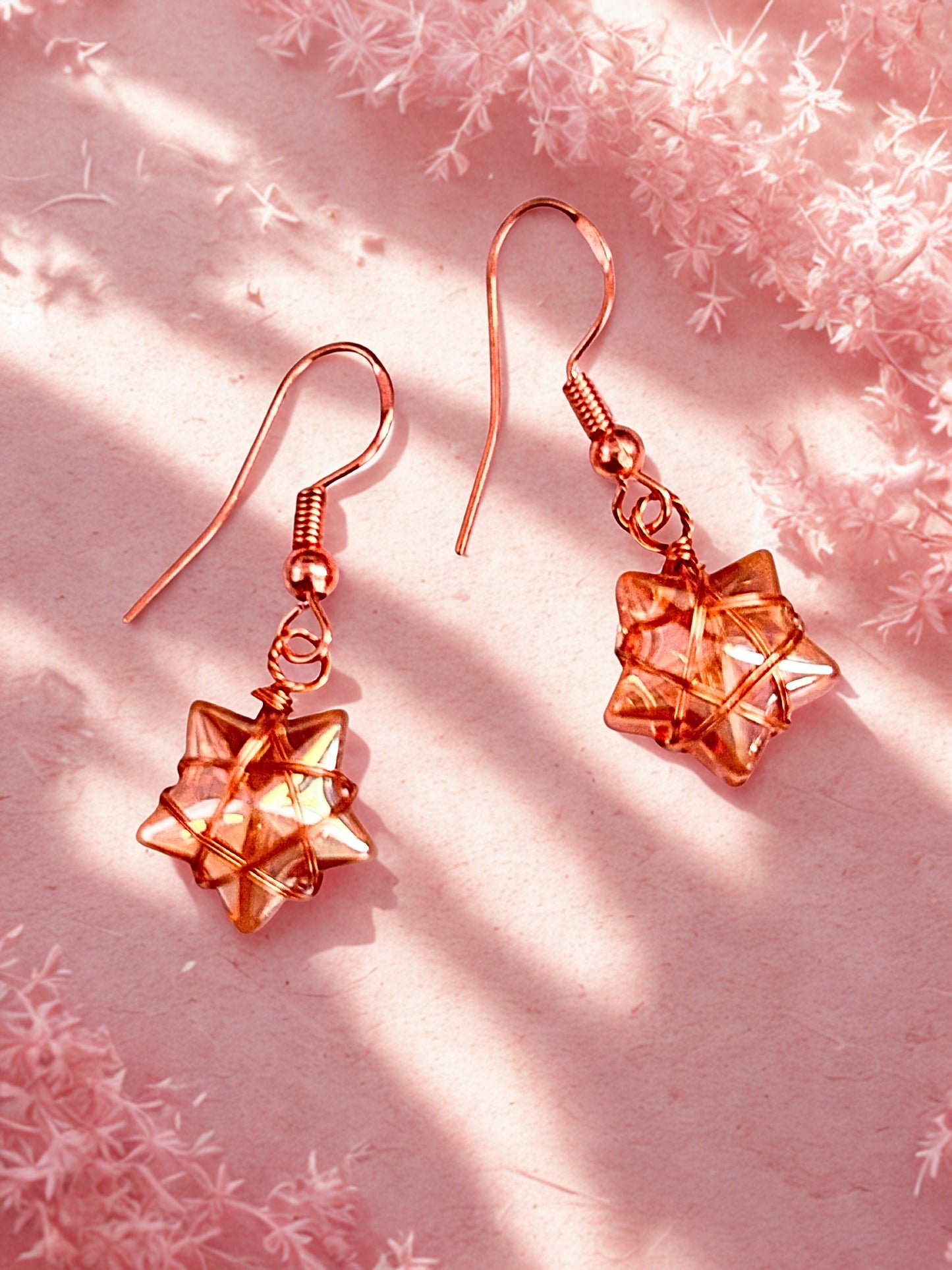 Rose gold star-shaped earrings on a pink textured background