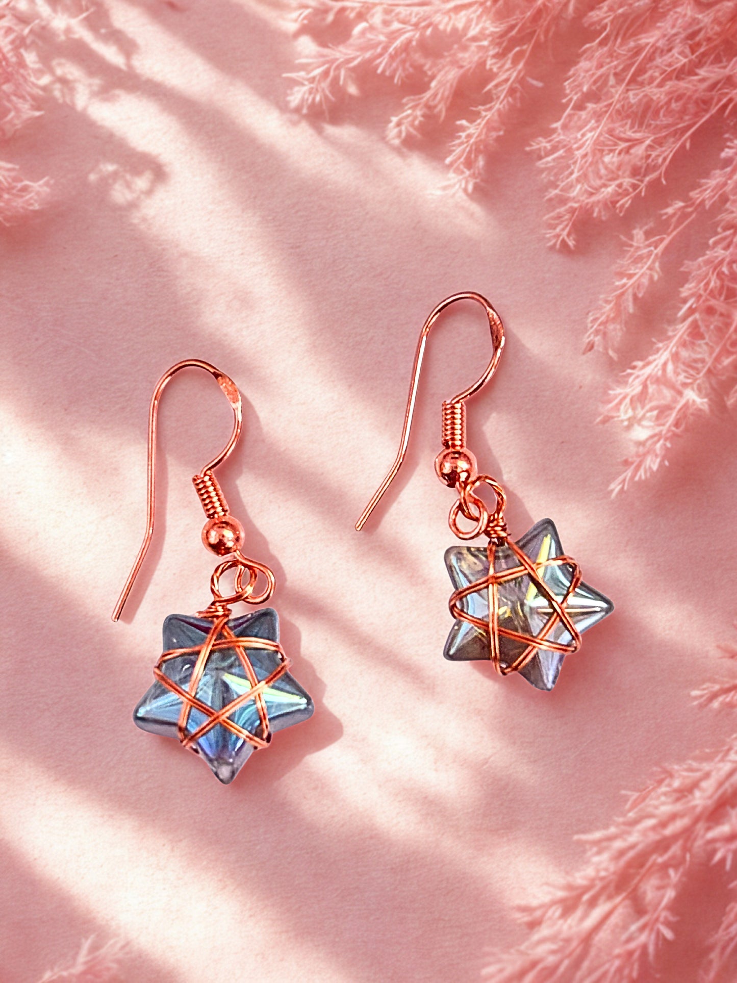 Star-shaped earrings with copper wire design on a pink background