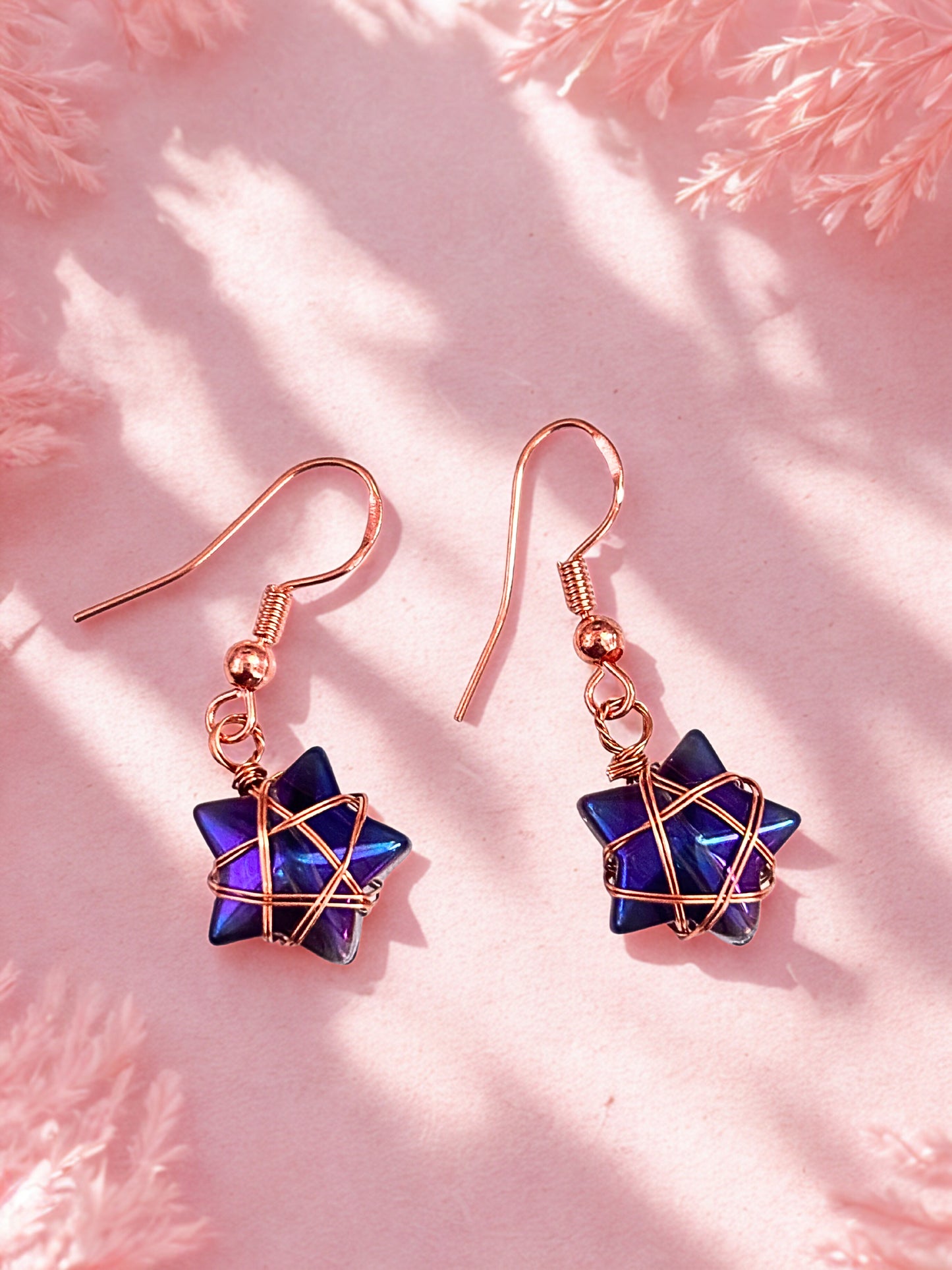 Star-shaped earrings with rose gold hooks on a pink surface