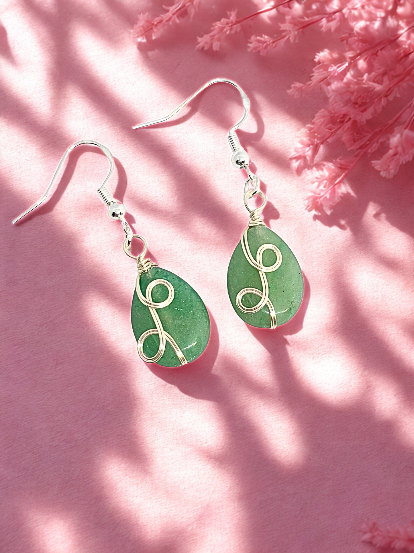 Green aventurine teardrop earrings with silver hooks on a pink background