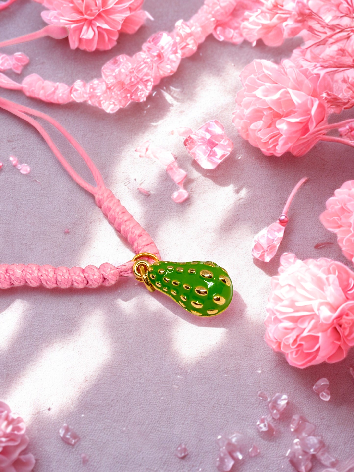 Pink cord bracelet with a green avocado charm on a pink floral background
