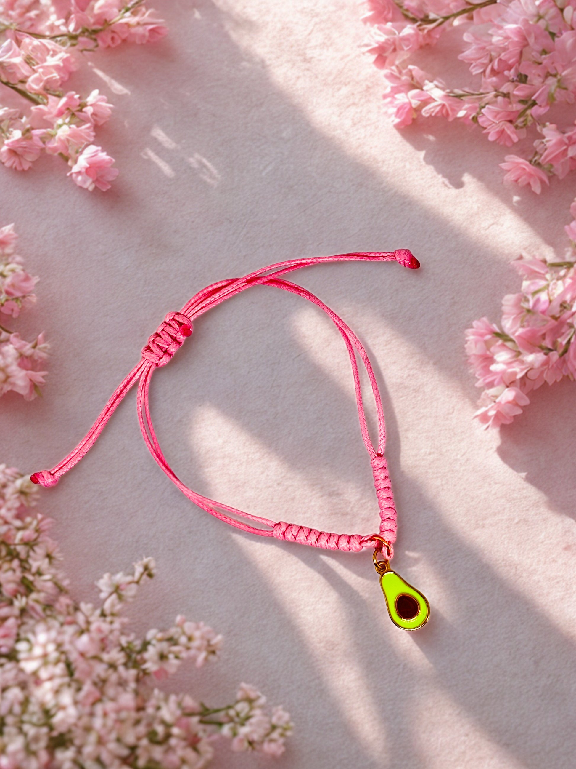 Pink bracelet with a green avocado charm on a light pink background with pink flowers