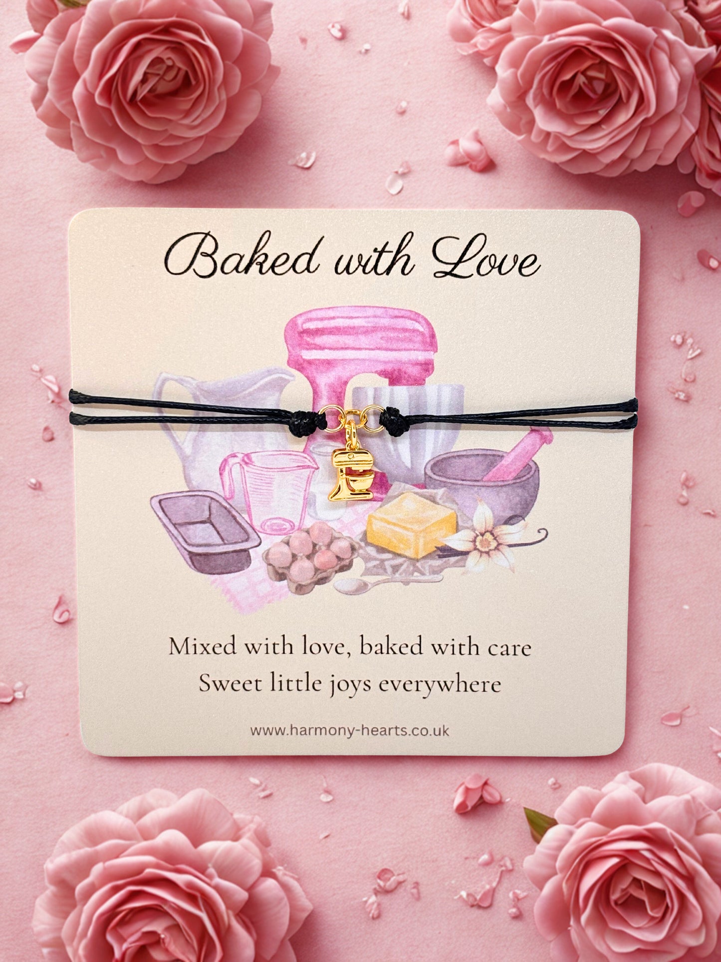 Card with baking-themed illustration and 'Baked with Love' text with a gold mixer charm bracelet on a pink floral background.
