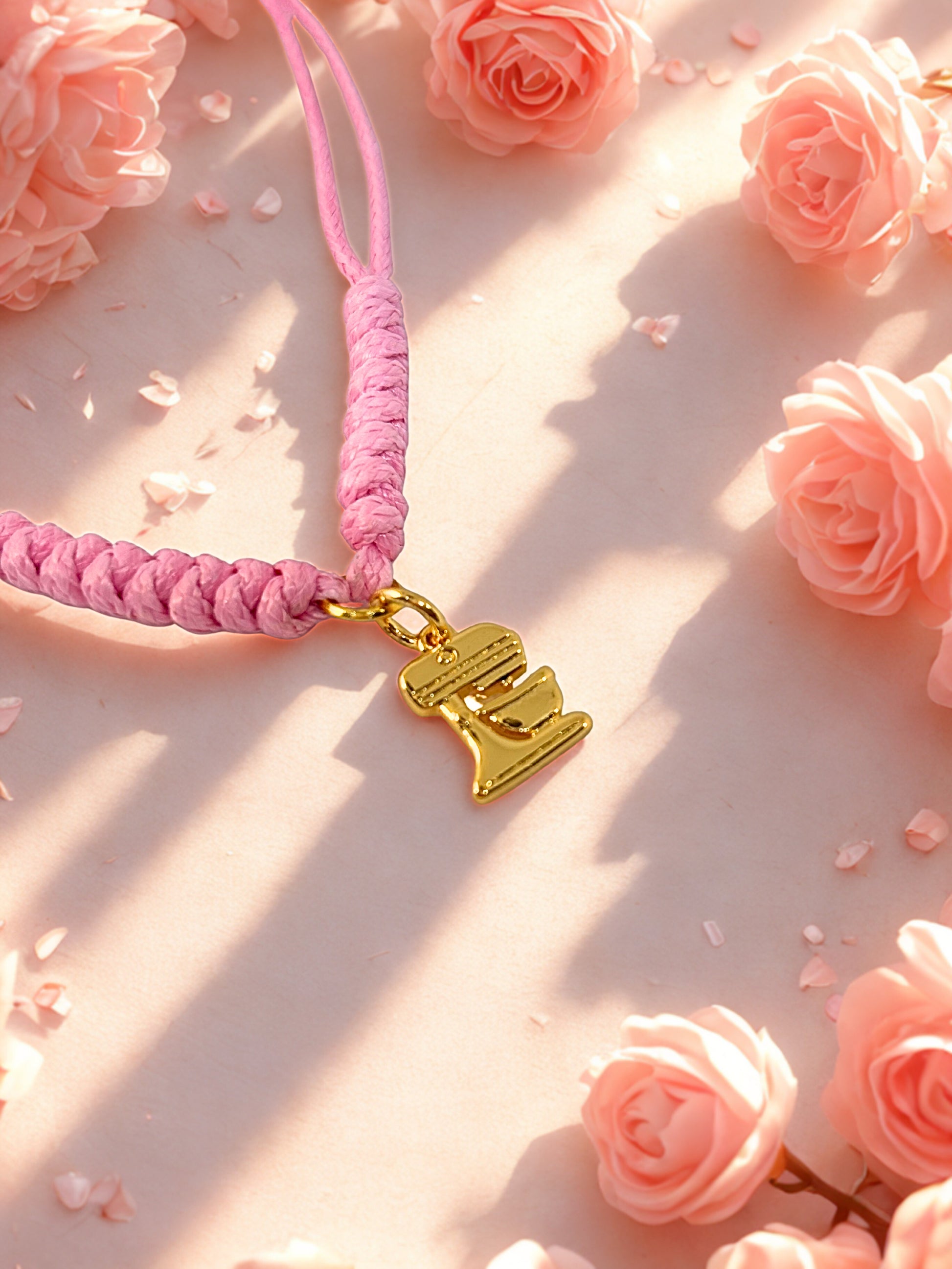 Pink braided bracelet with a gold pmixer charm on a pink floral background