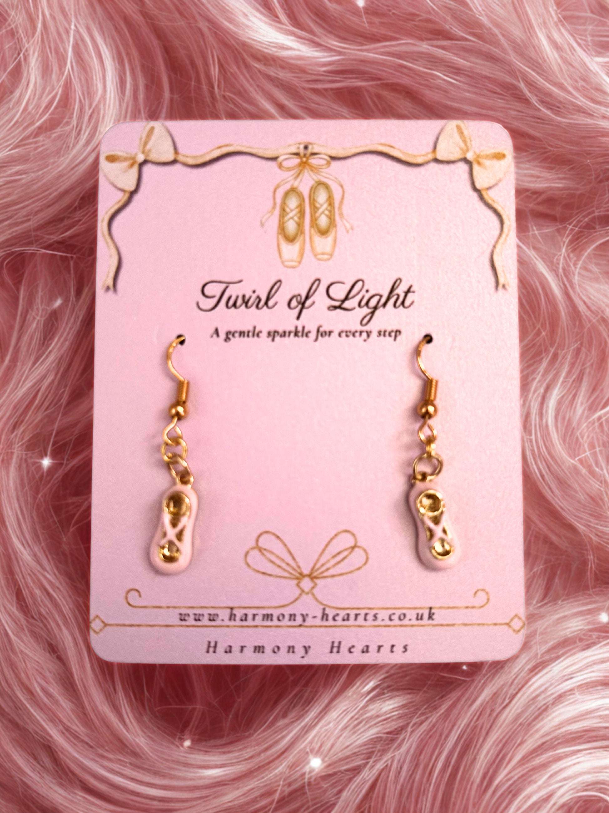 Gold ballet slipper earrings on a pink card with 'Harmony Hearts' branding against a pink fluffy background.