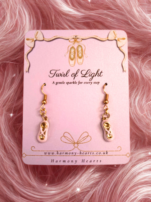 Gold ballet slipper earrings on a pink card with 'Harmony Hearts' branding against a pink fluffy background.