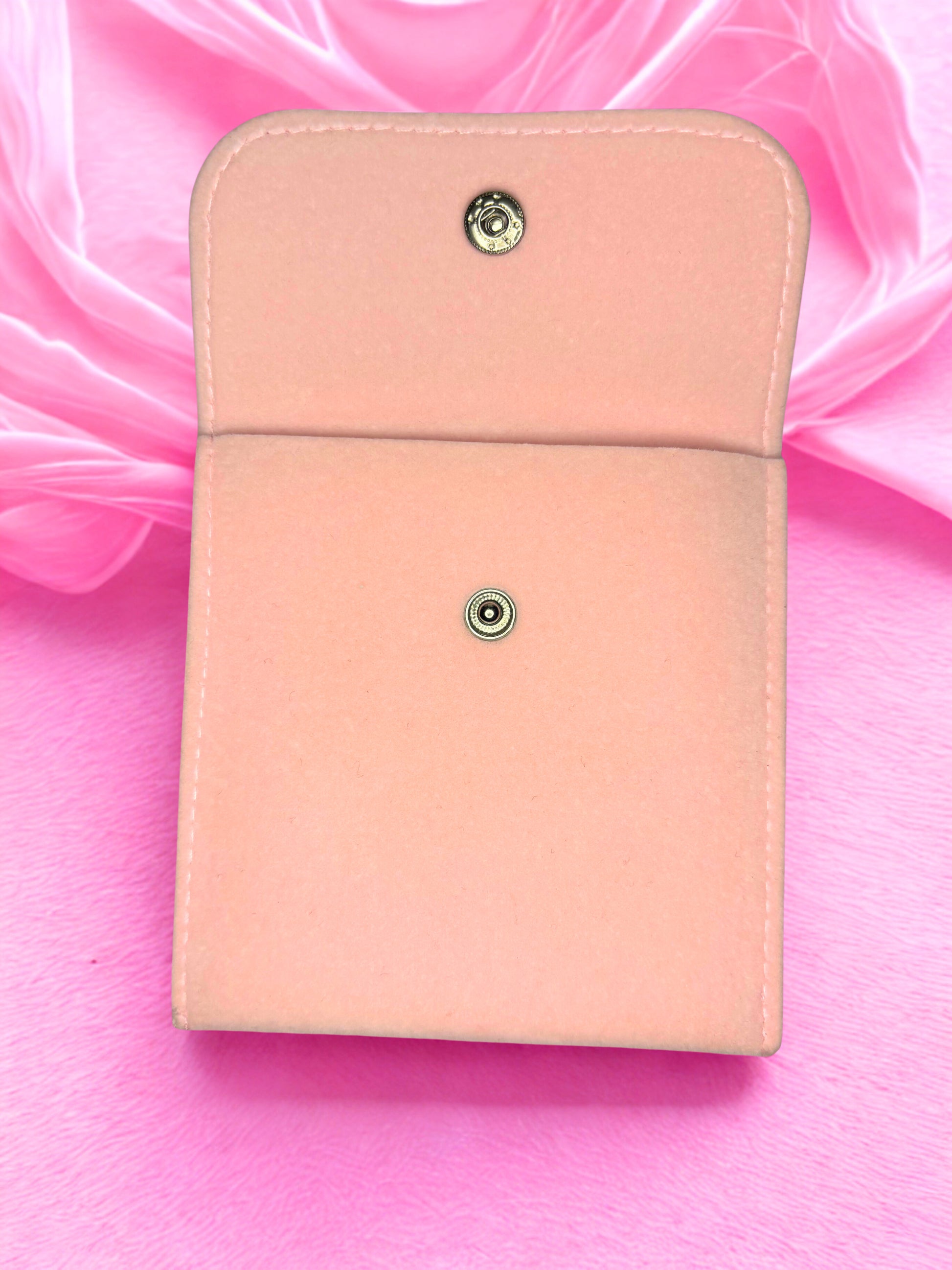 Pink leather wallet with two metal buttons on a pink fabric background