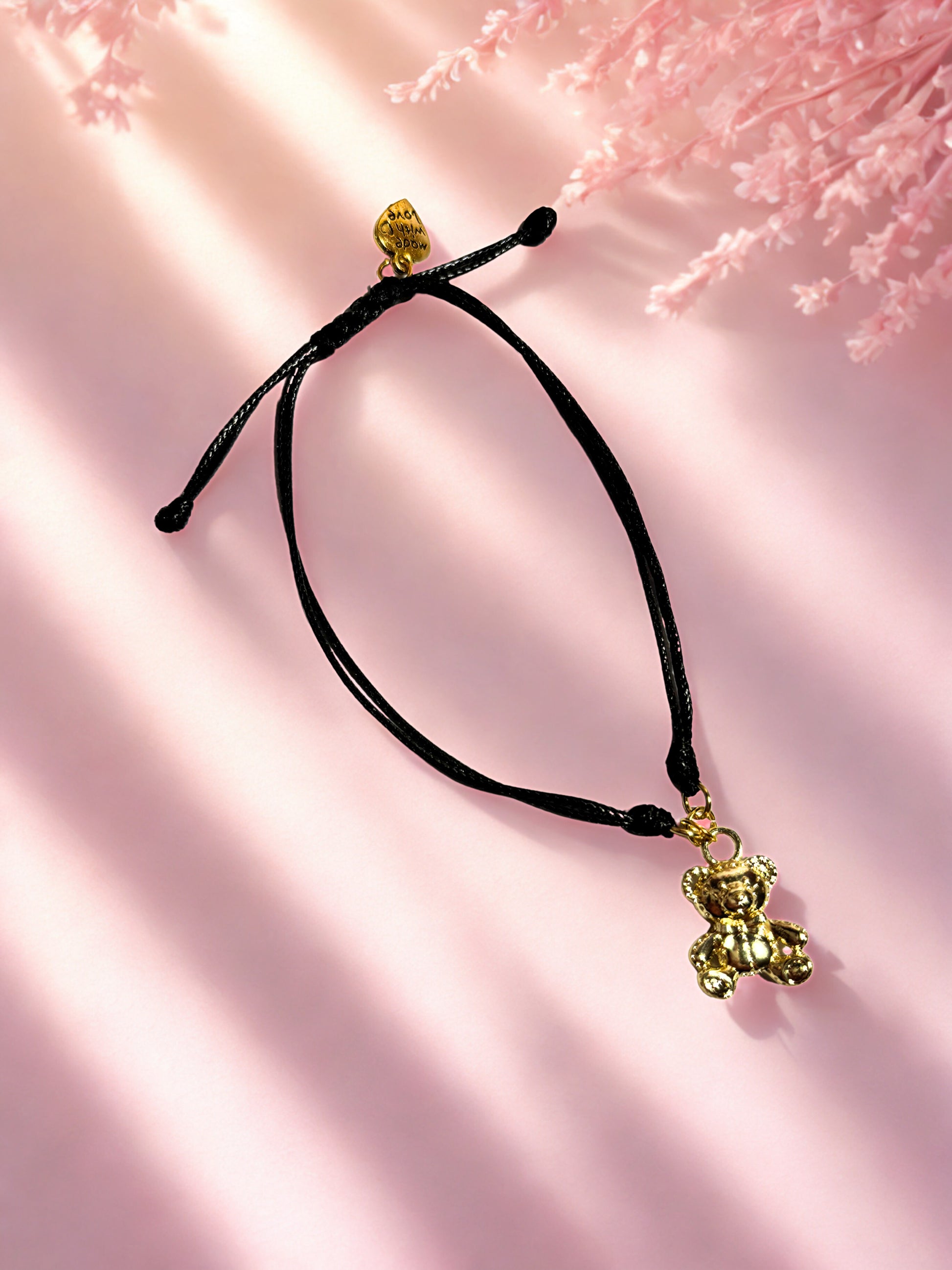 Black cord bracelet with gold bear charm on a pink background