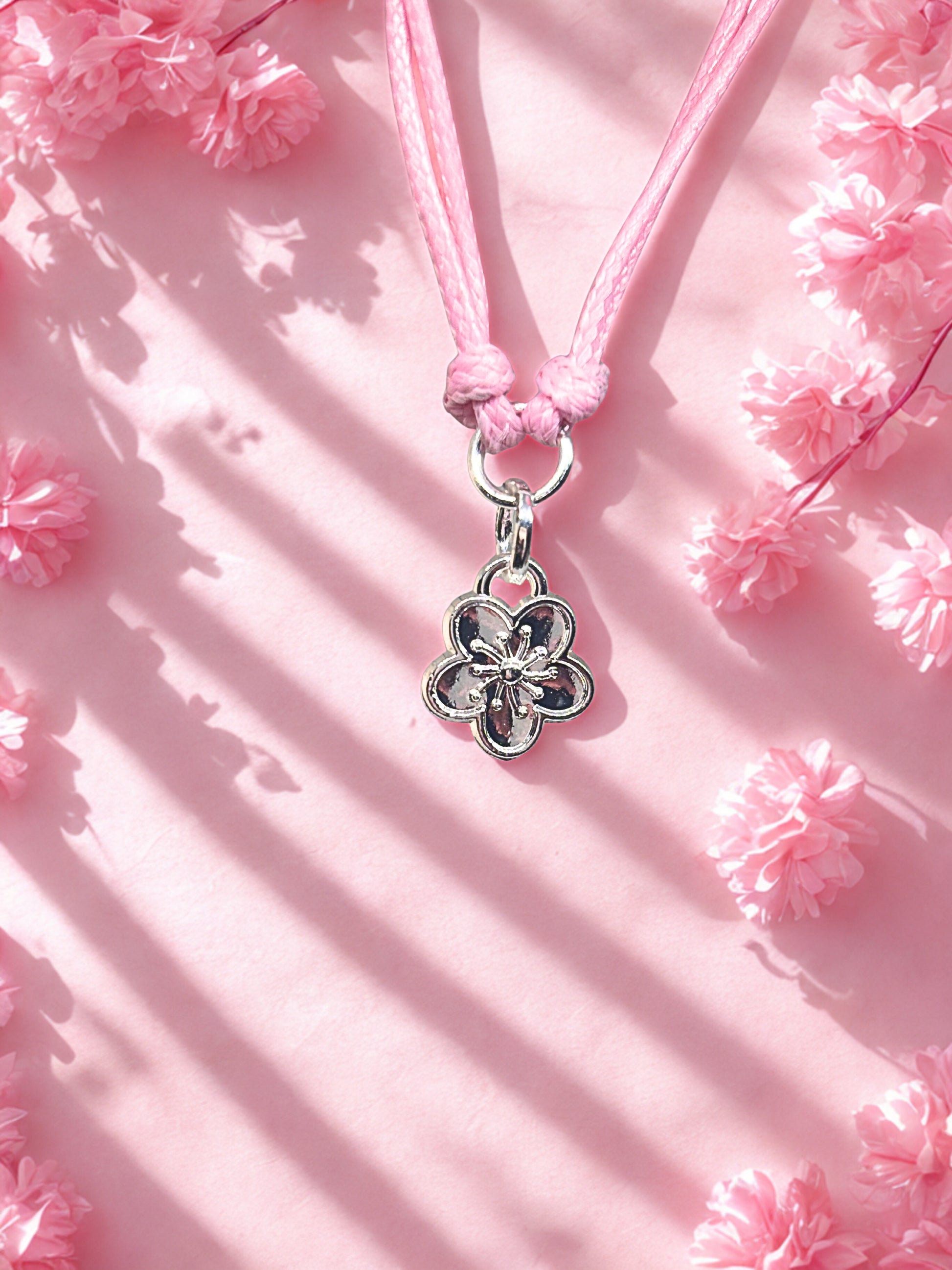 Pink cord bracelet with a silver flower charm on a pink floral background